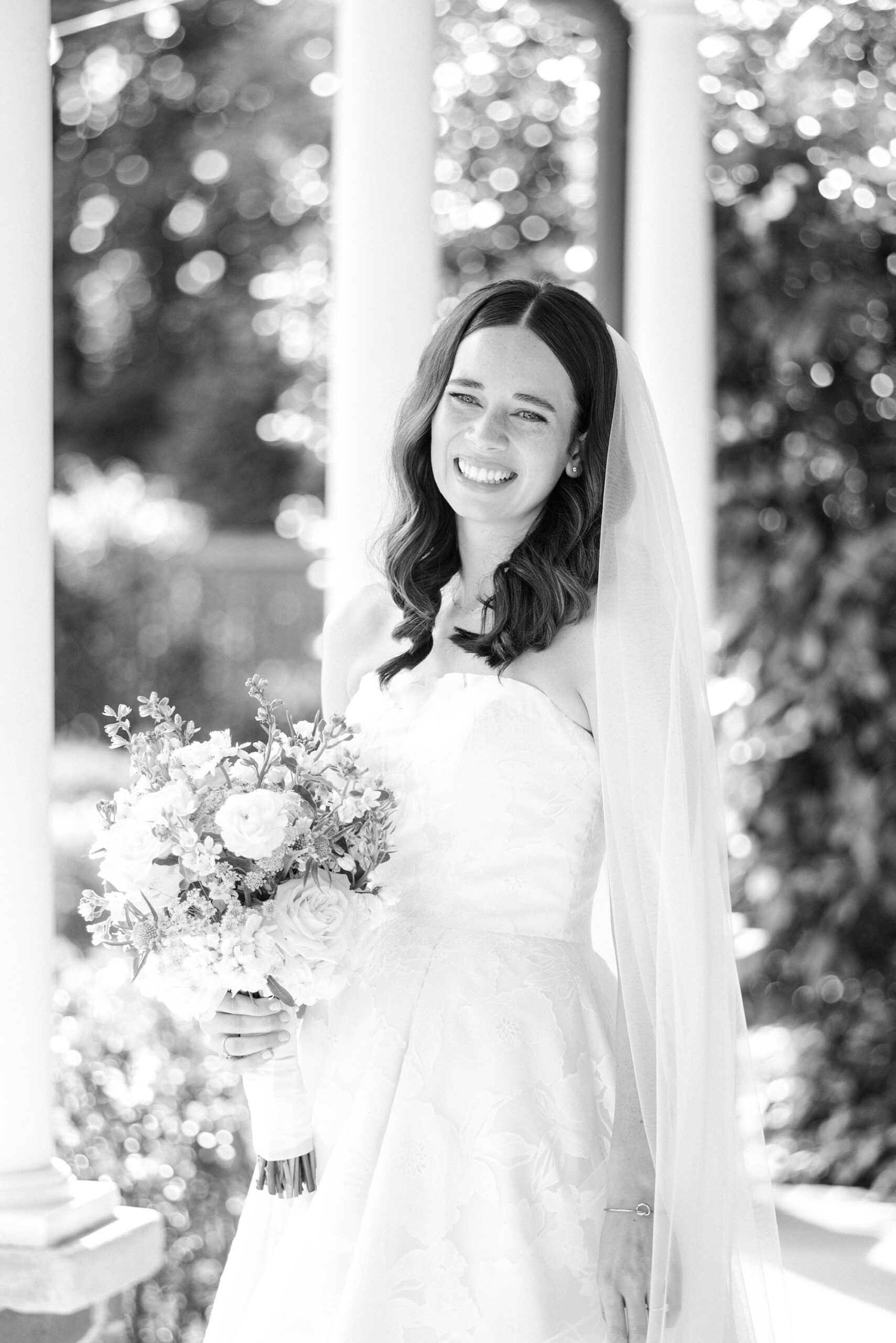 bride laughs holding bouquet of white flowers on porch of Alexander Homestead