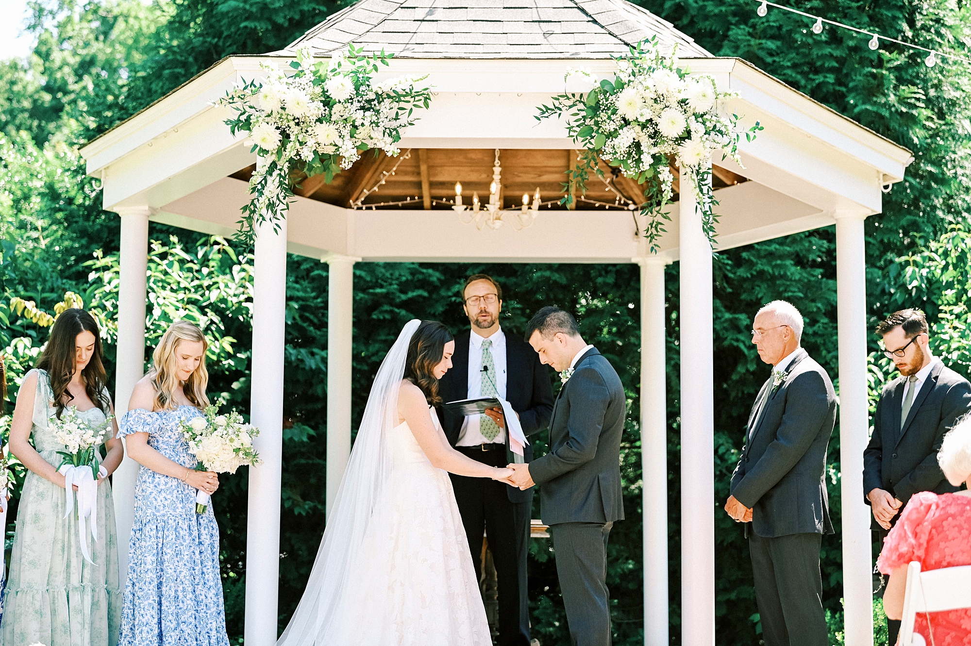 newlyweds bow heads in prayer during wedding ceremony in gazebo at Alexander Homestead