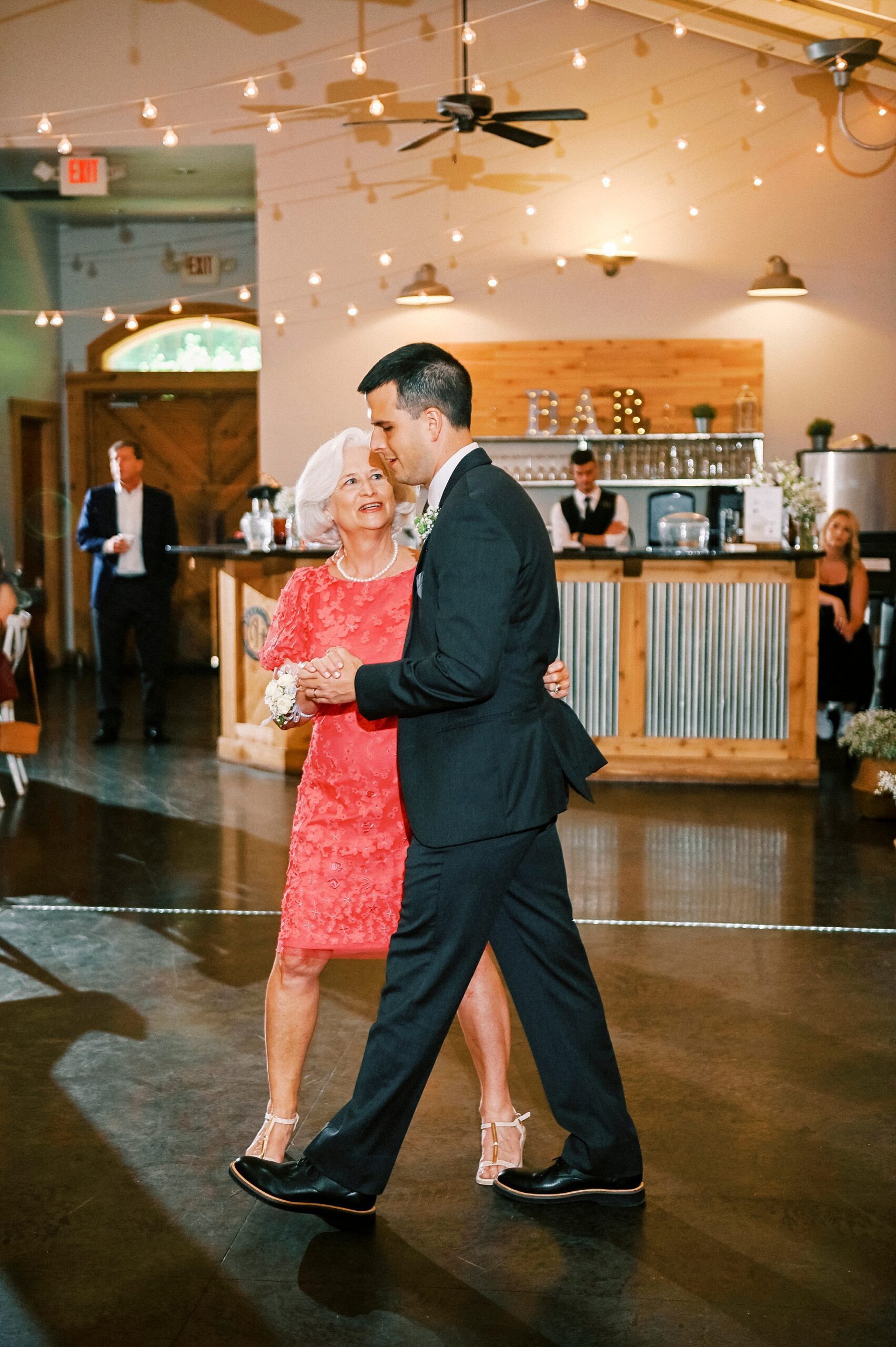 groom dances with mother in red dress at brunch wedding reception at Alexander Homestead