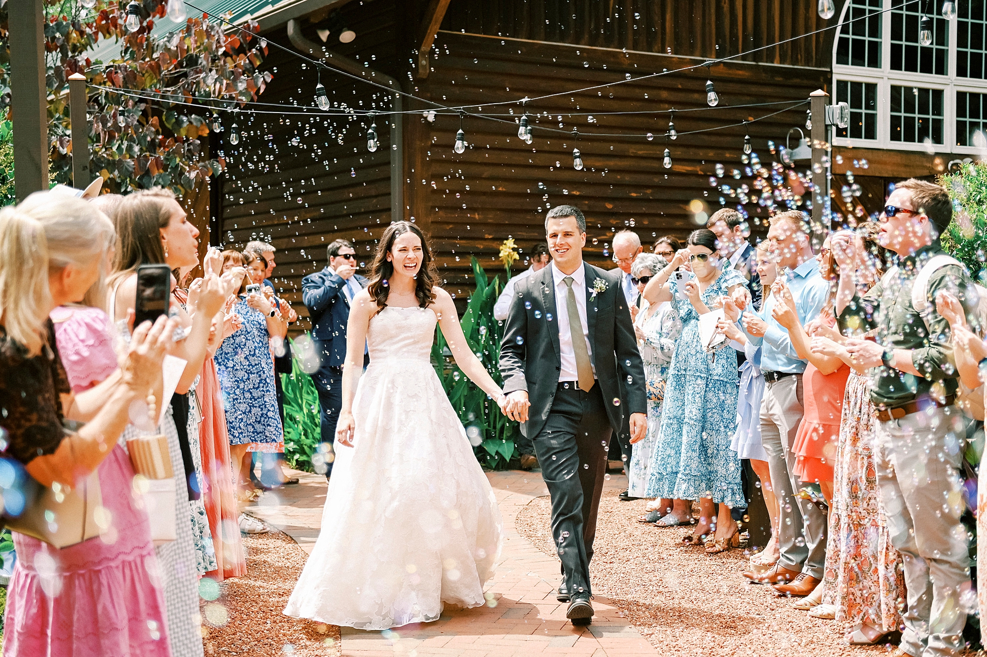 newlyweds hold hands walking through bubbles at Alexander Homestead
