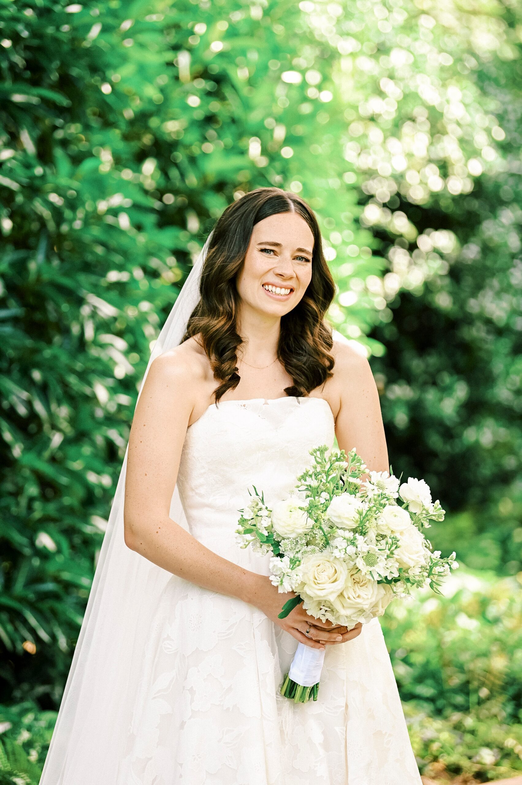 brunette bride smiles holding bouquet of flowers in front of her gown
