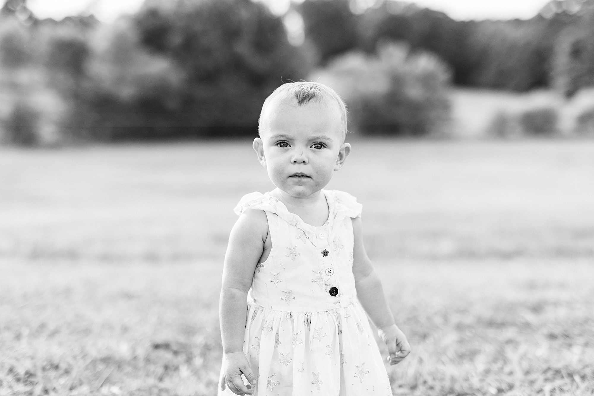 one year old stands in white dress in field of farm