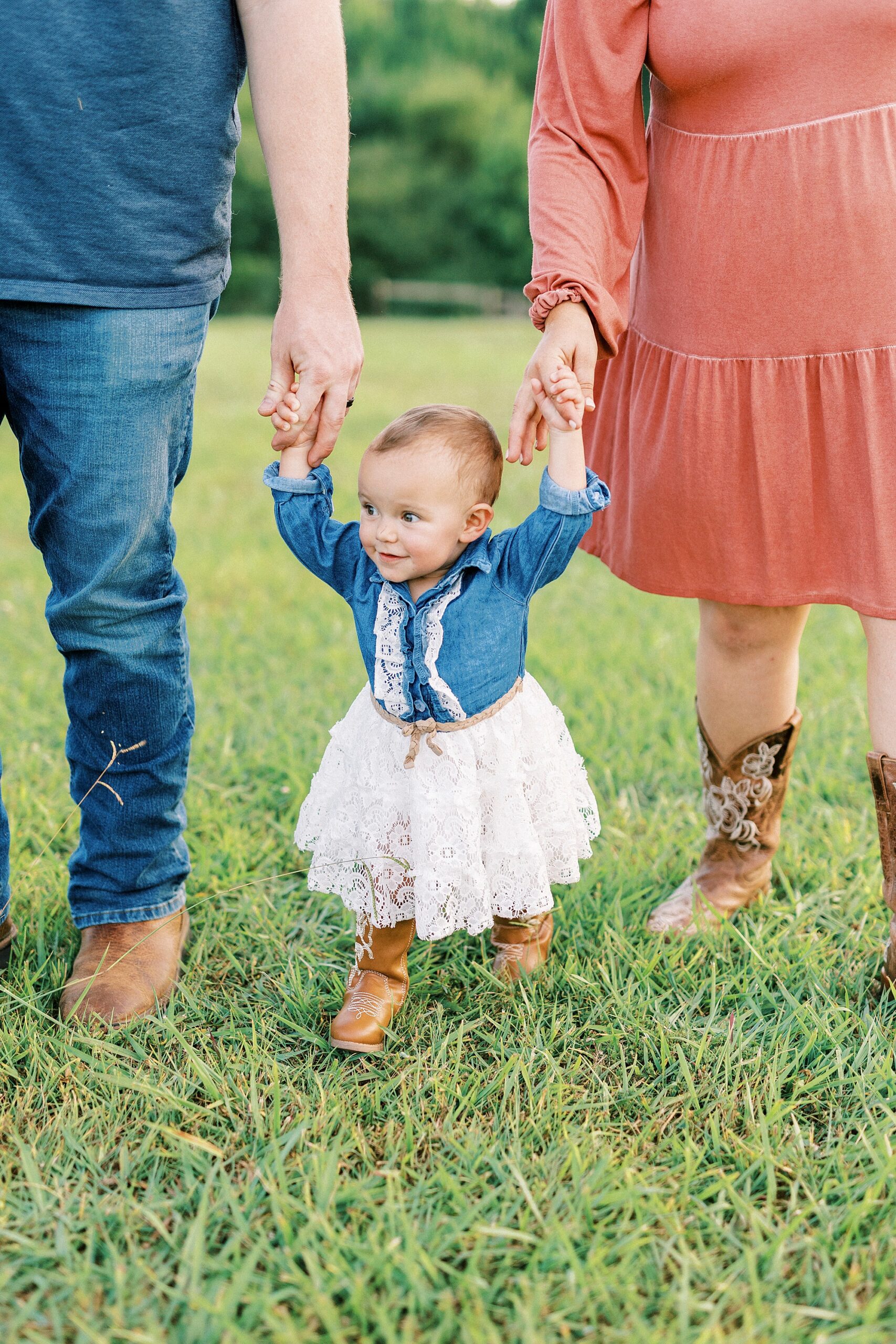 couple holds hands with daughter walking on family farm in Albemarle NC during first birthday portraits