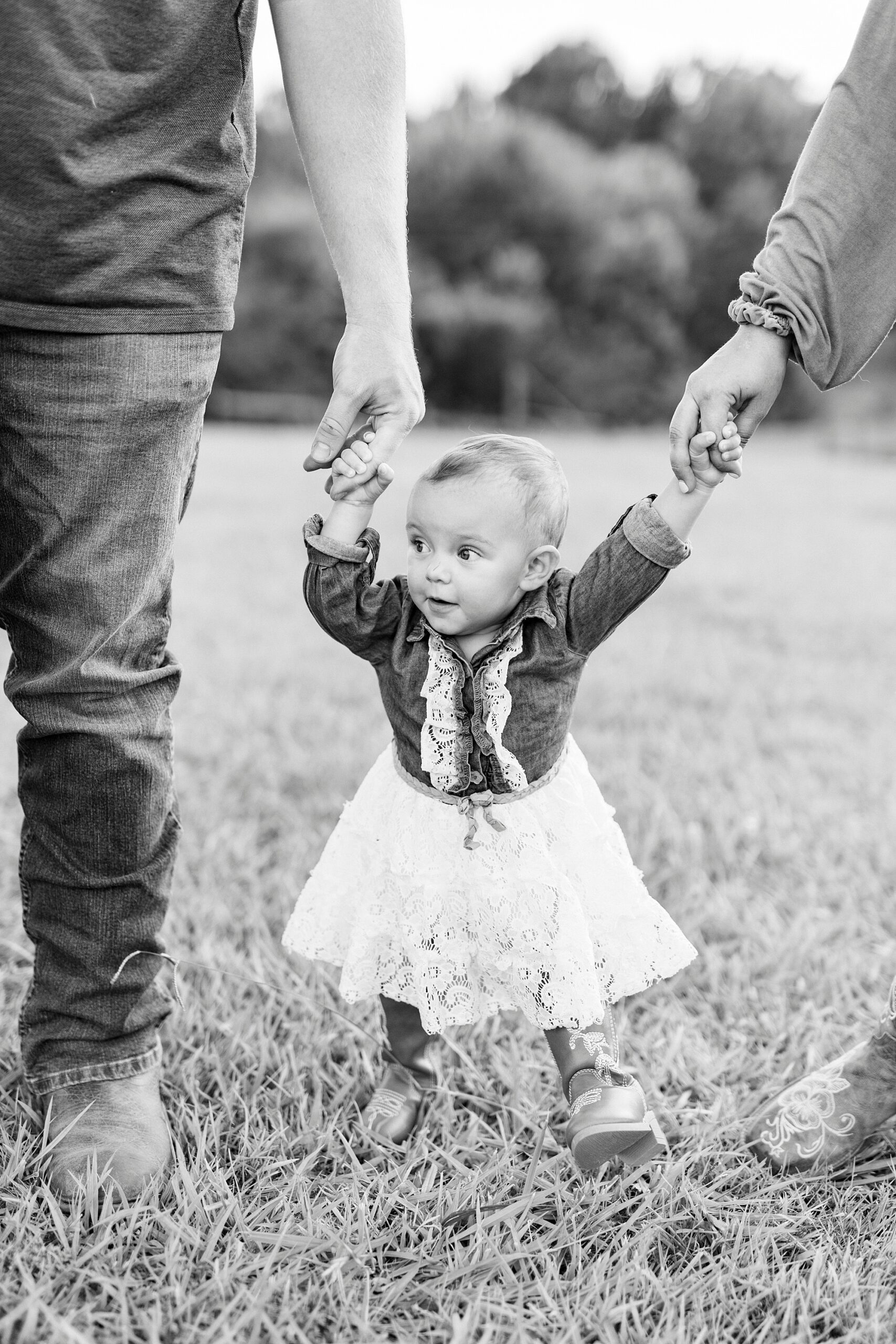 mom and walk holding toddler's hand across grass during first birthday portraits in Albemarle NC