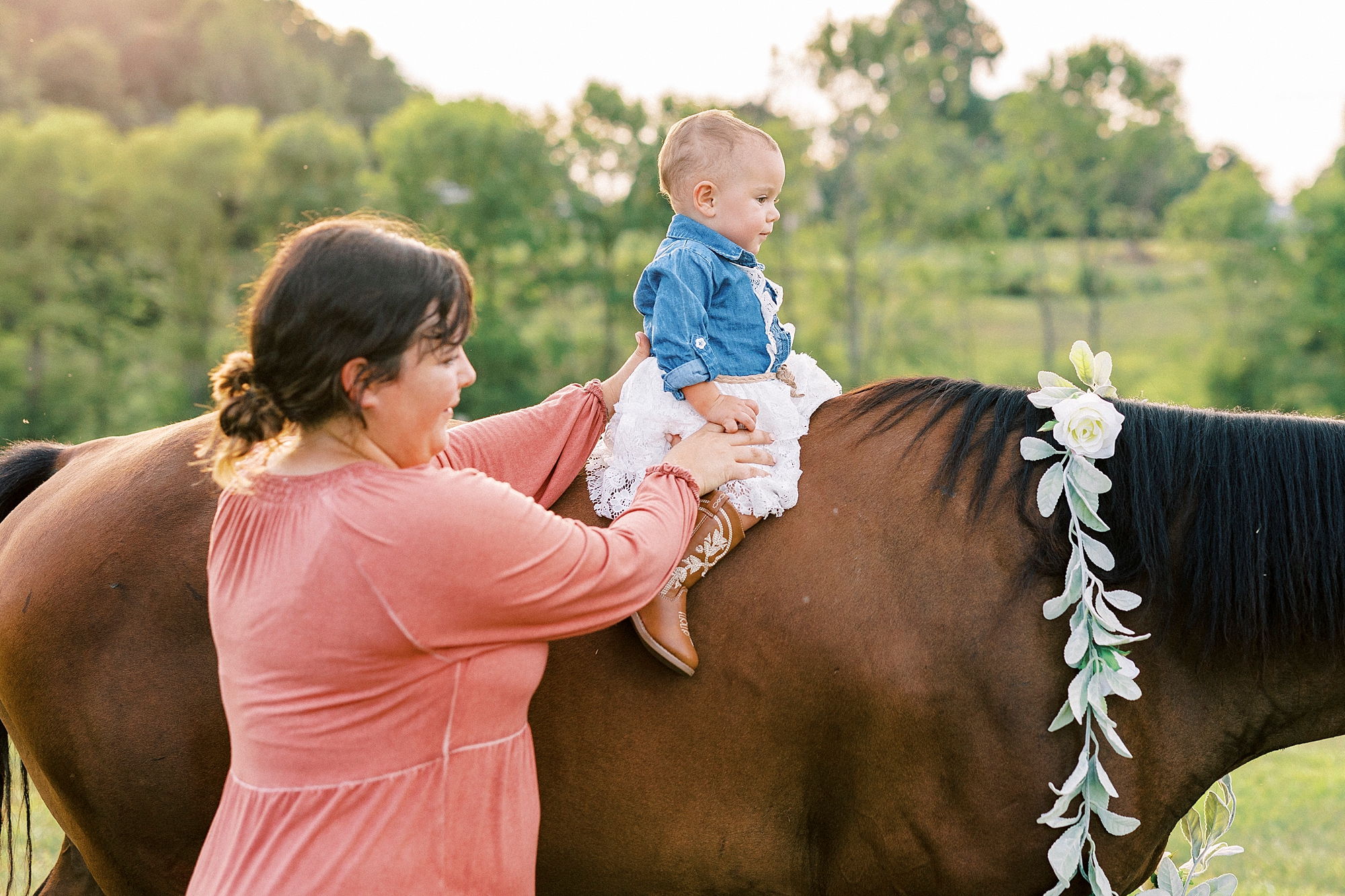 mom in coral dress holds one year old daughter on back of brown horse in Albemarle NC
