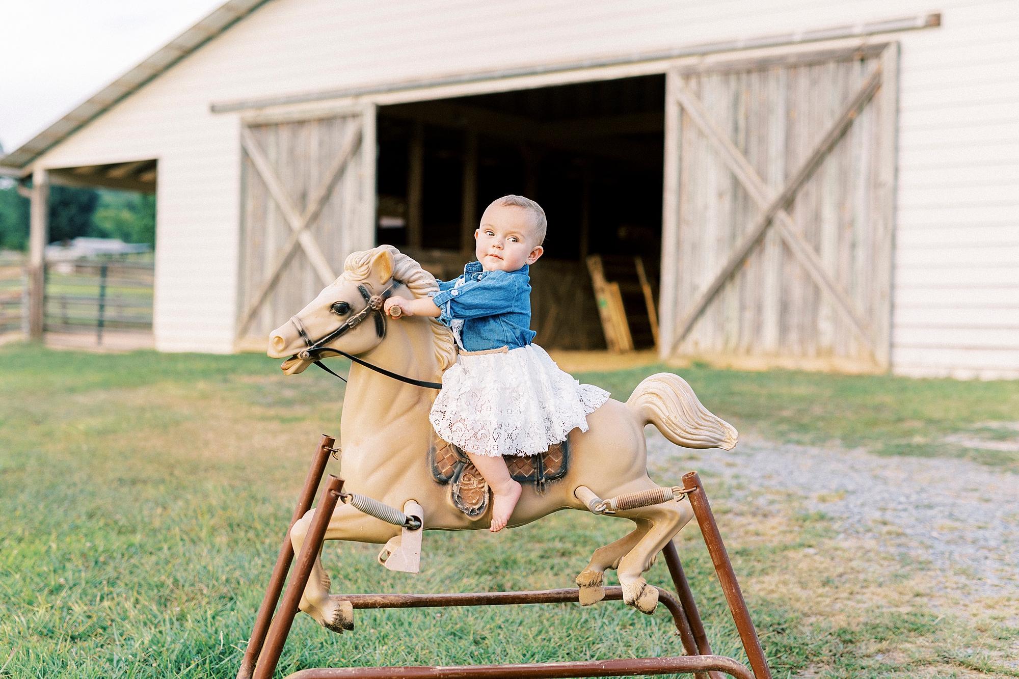 toddler rides vintage rocking horse in front of wooden barn