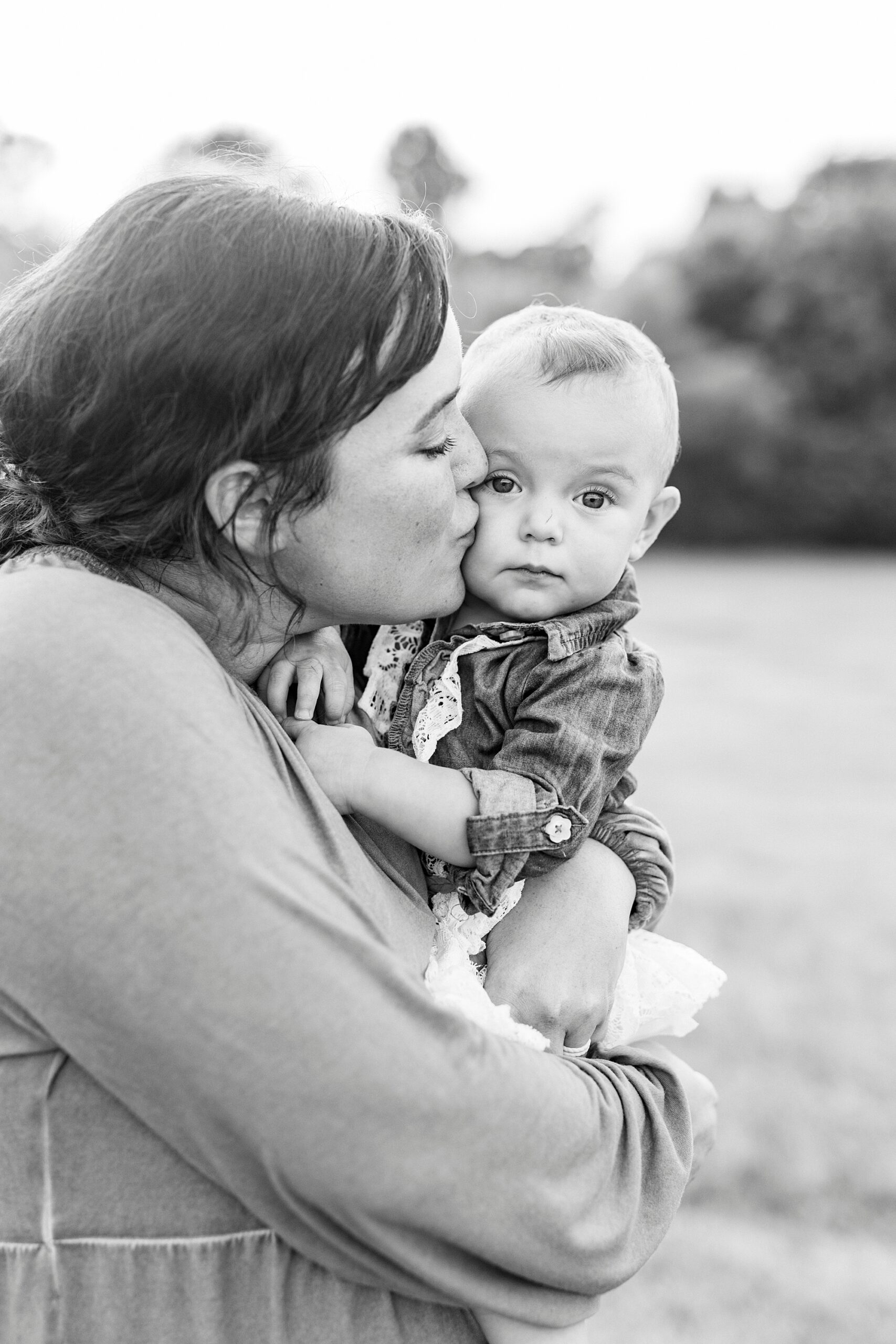 mom hugs one year old and kisses her cheek during first birthday portraits in Albemarle NC