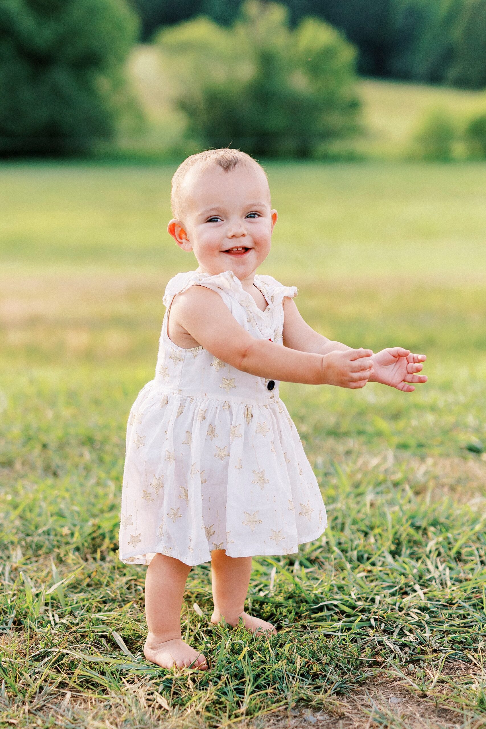toddler in white dress claps hand in field of family farm