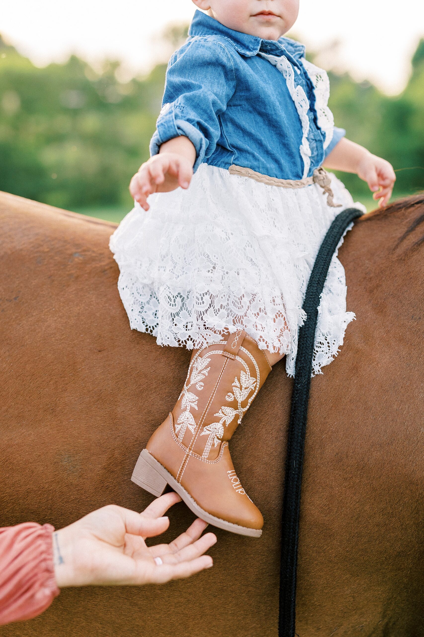 toddler rides horse while mom holds her heel in cowboy boots