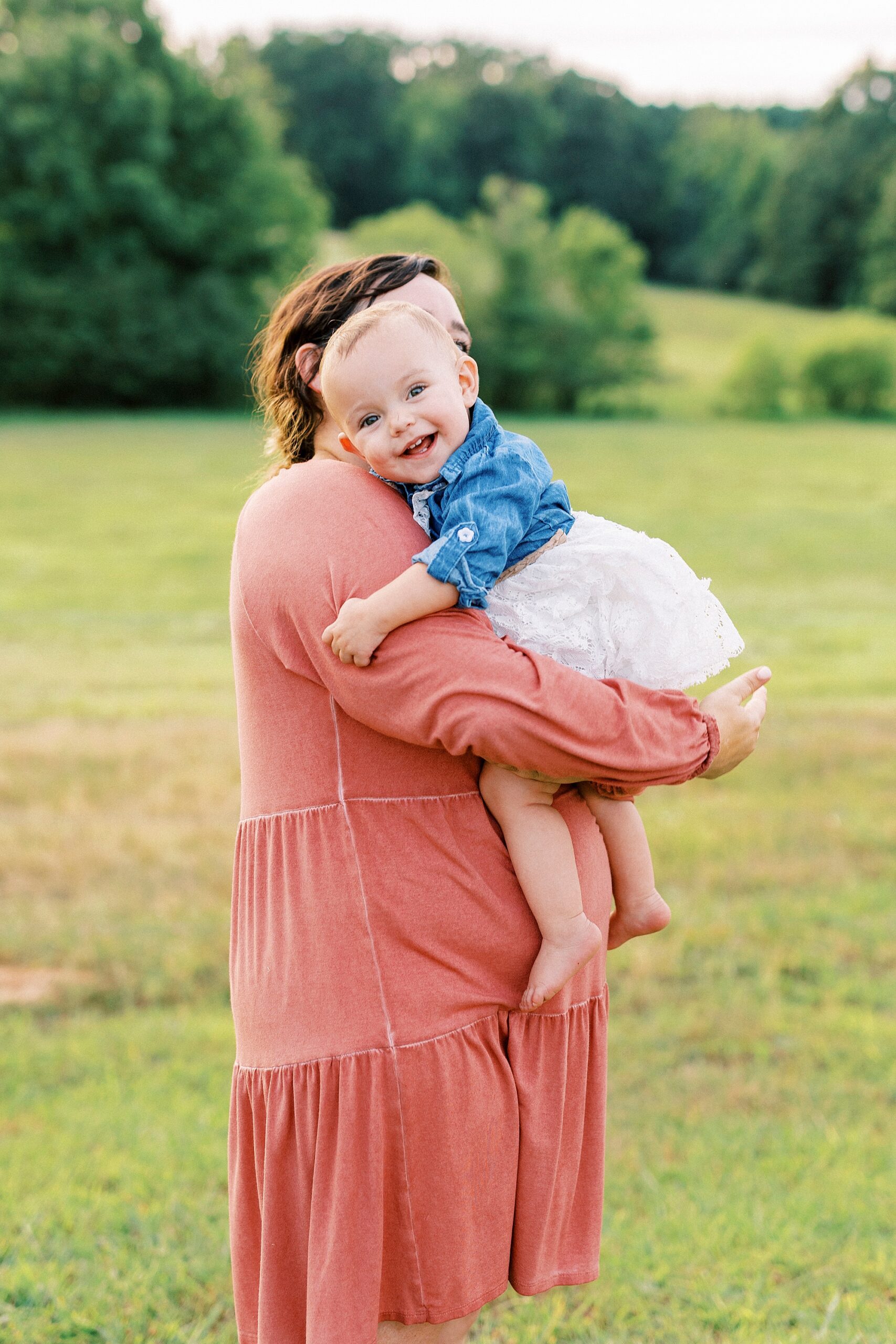 toddler lays on mom's arm smiling during first birthday portraits in Albemarle NC