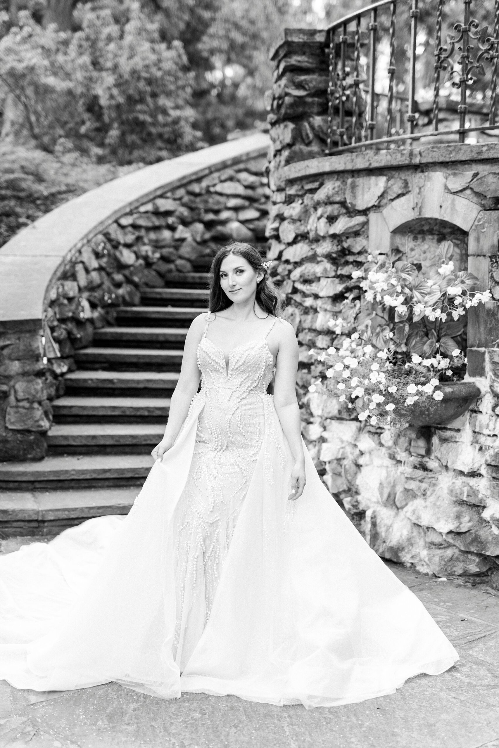 bride stands in front of stone staircase with wedding gown with extra train panels around her