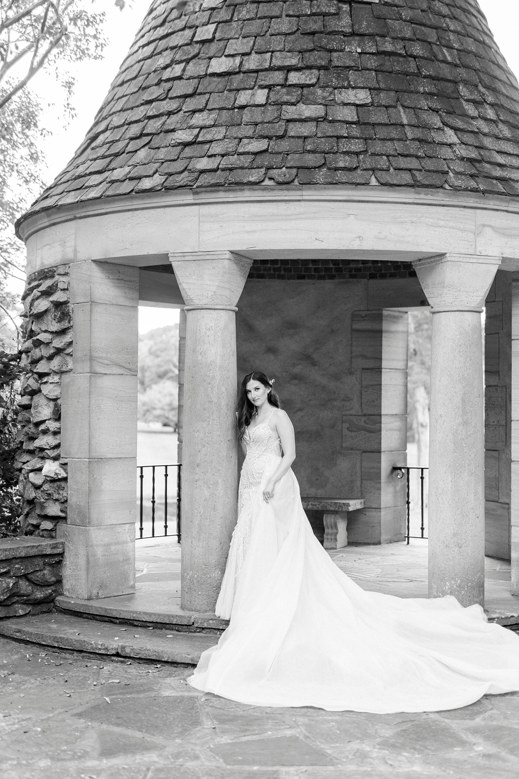 bride leans against the stone pillar of the gazebo at the Graylyn Estate