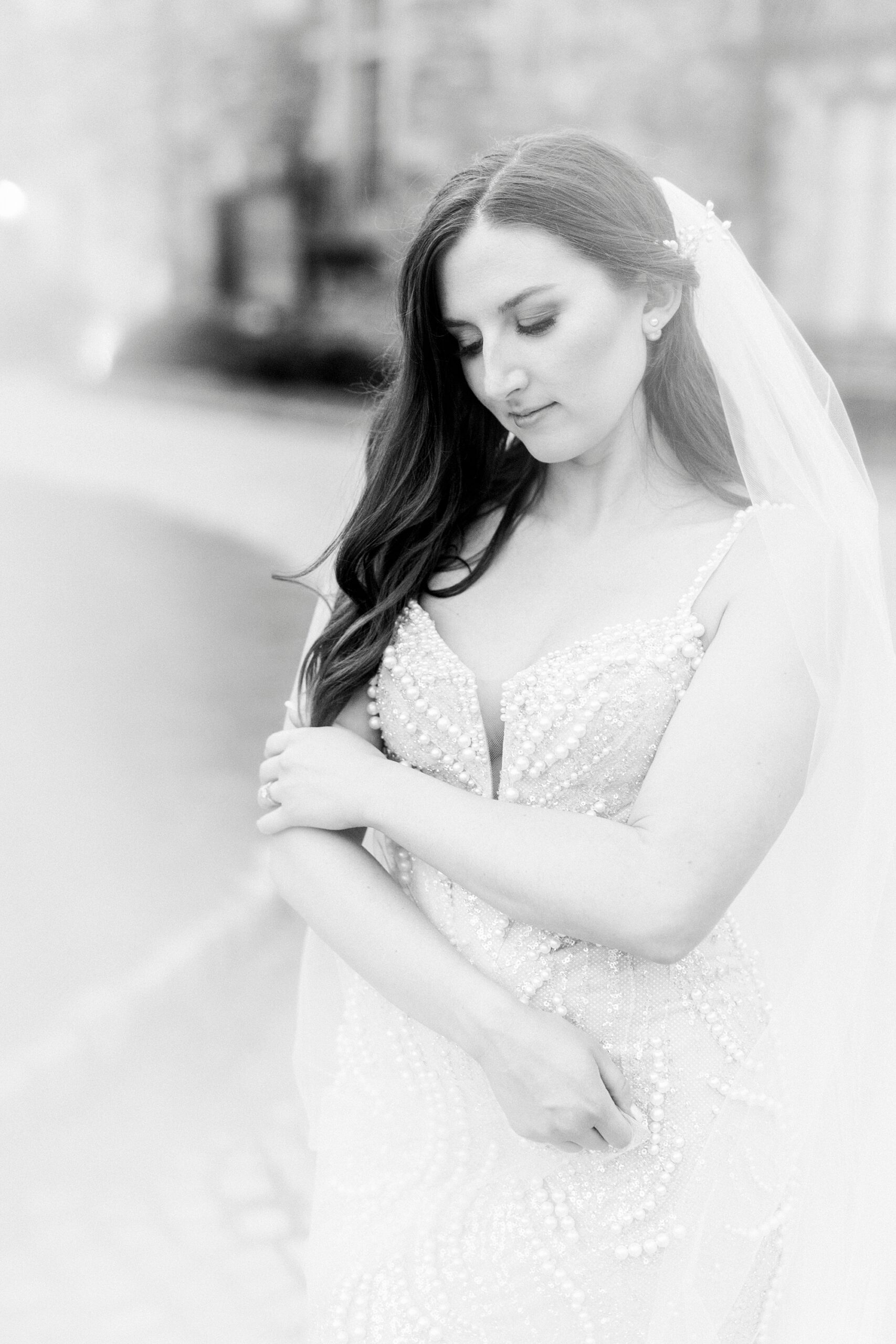 bride holds her arms across her chest looking down with her veil behind her