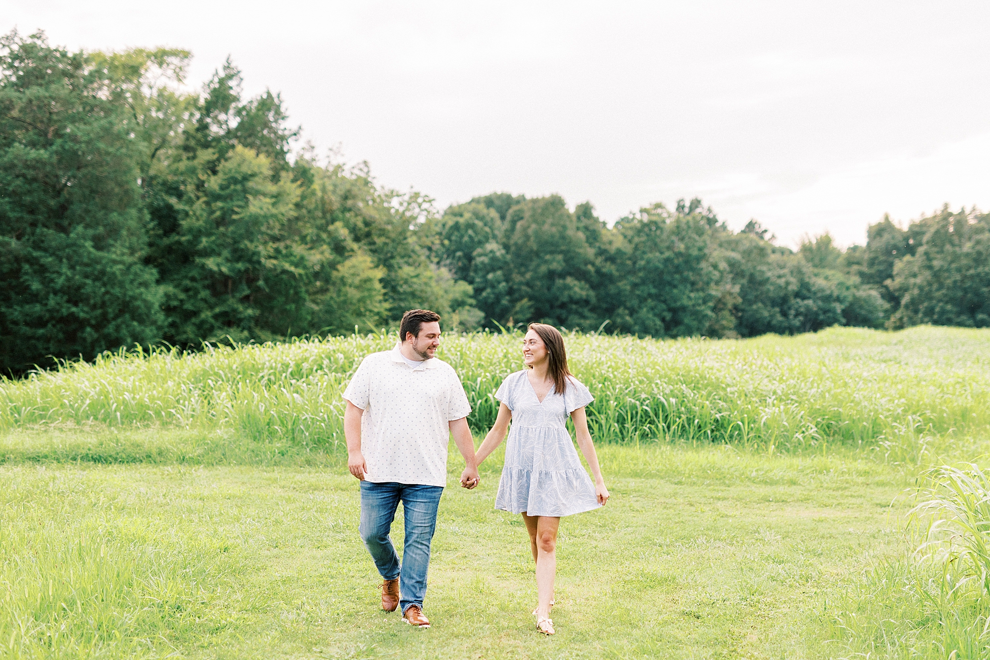 man and woman hold hands walking through fields during Kannapolis NC engagement session