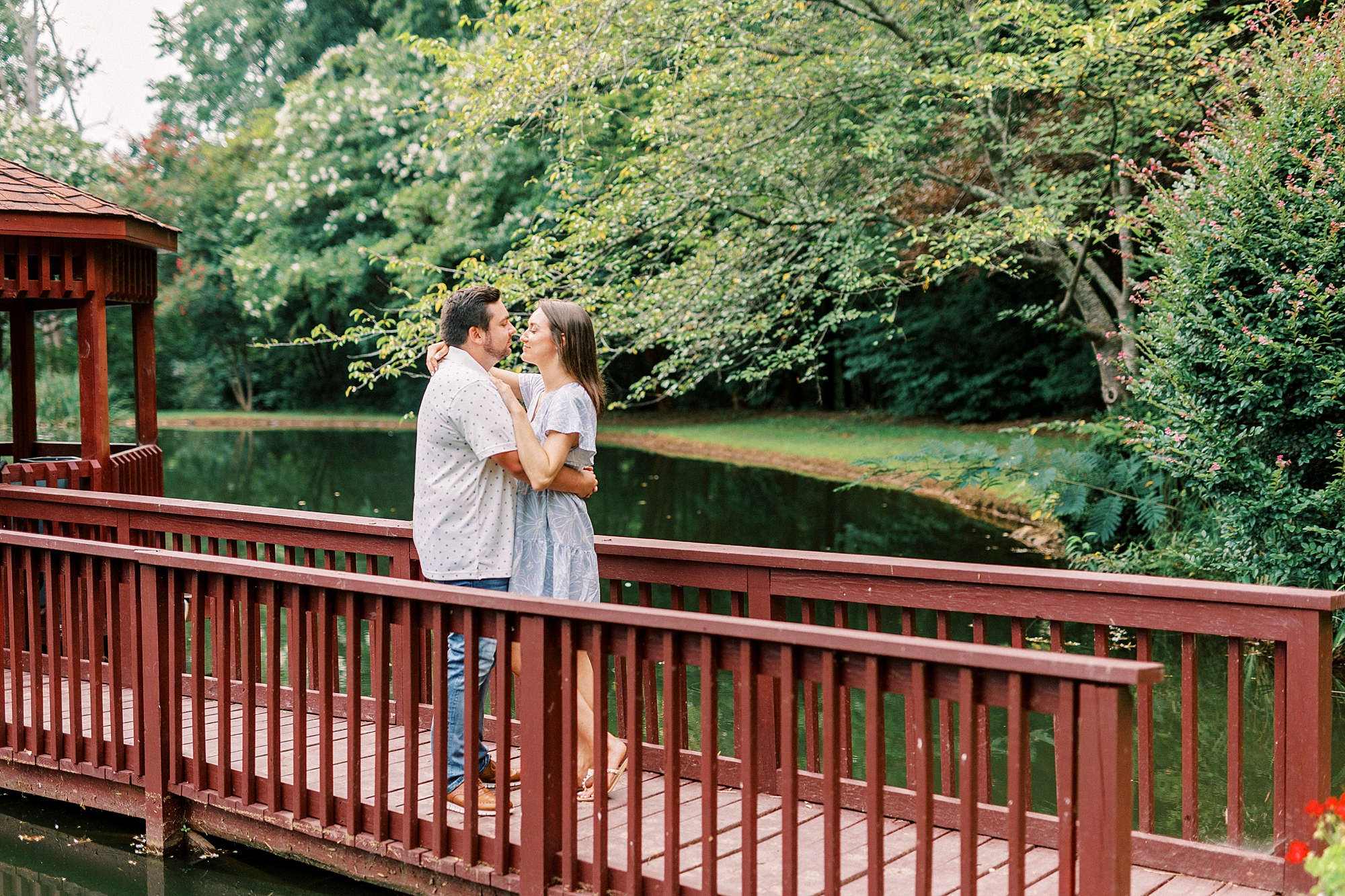 engaged couple hugs on red wood bridge outside home 