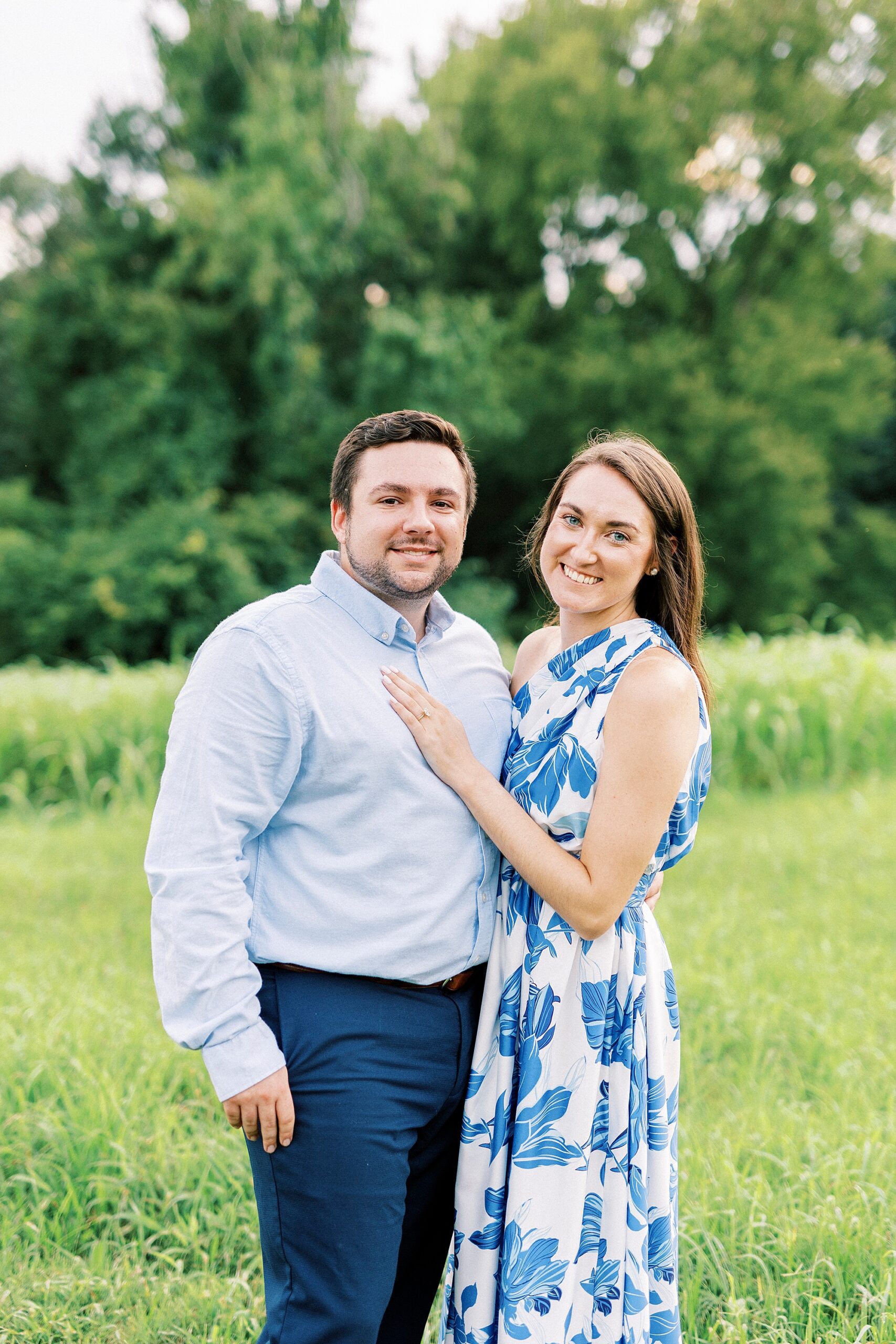 woman stands with hand on man's chest showing off engagement ring 