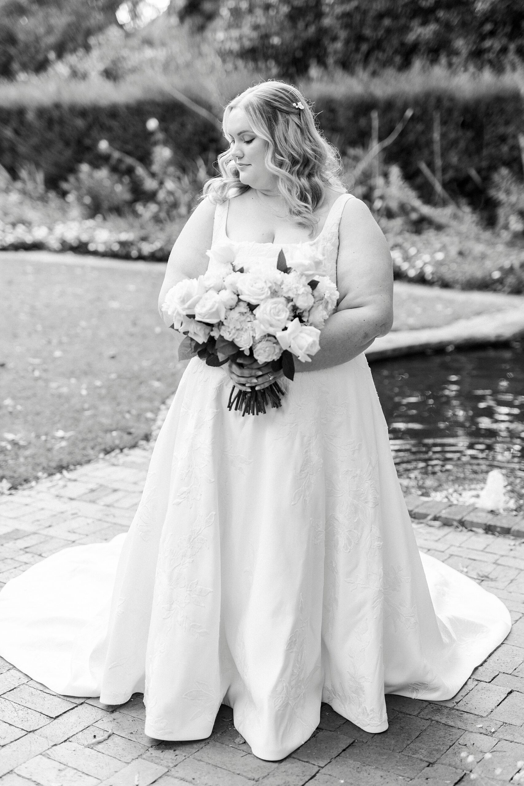 bride stands by pond inside Wing Haven Gardens holding bouquet 