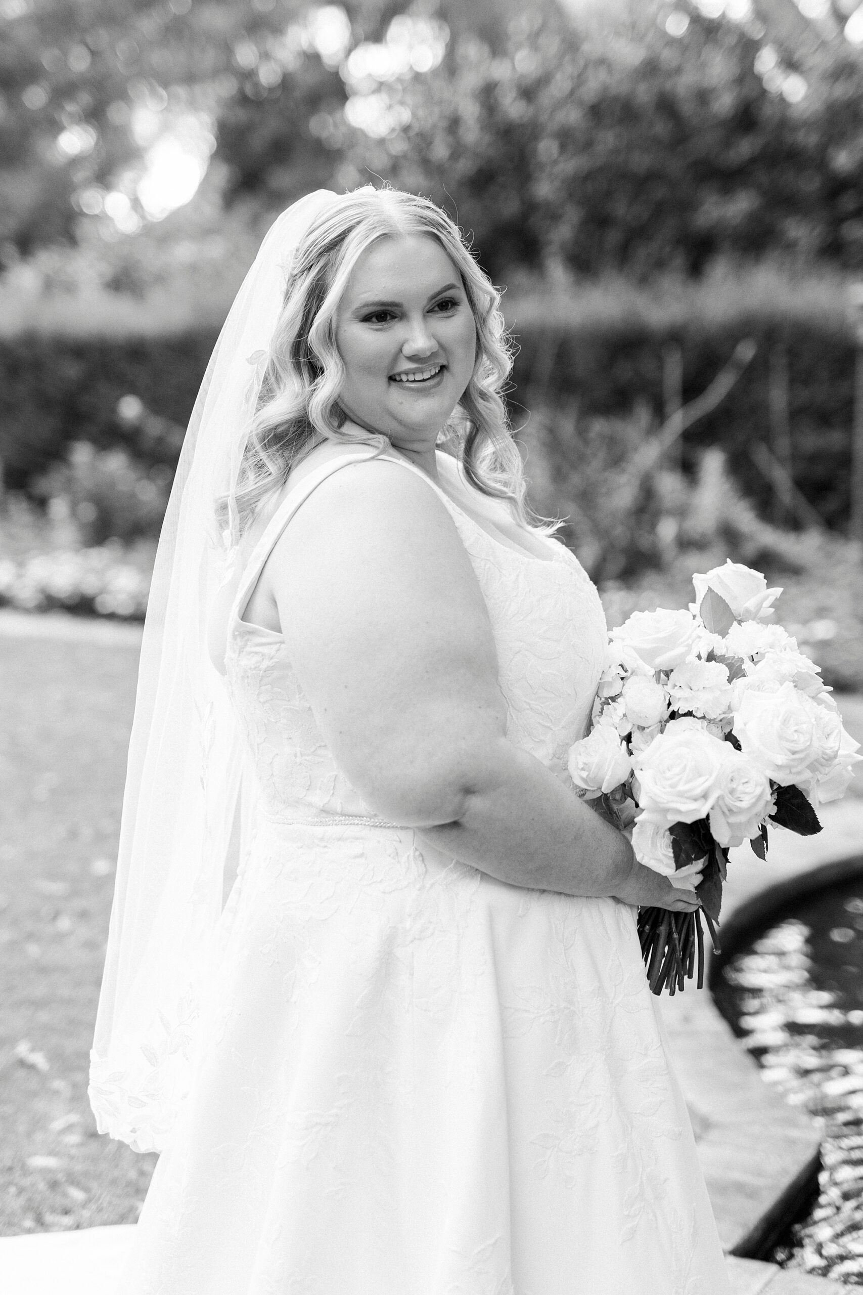 bride smiles over shoulder holding bouquet of white flowers 