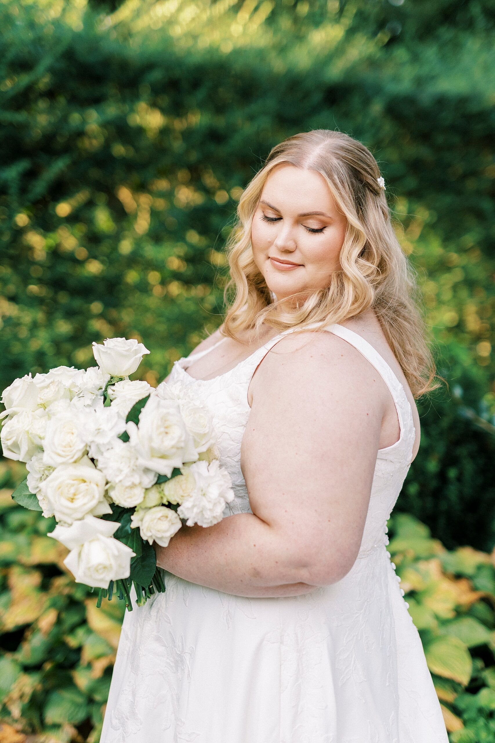 bride smiles looking down at ivory roses inside Wing Haven Gardens