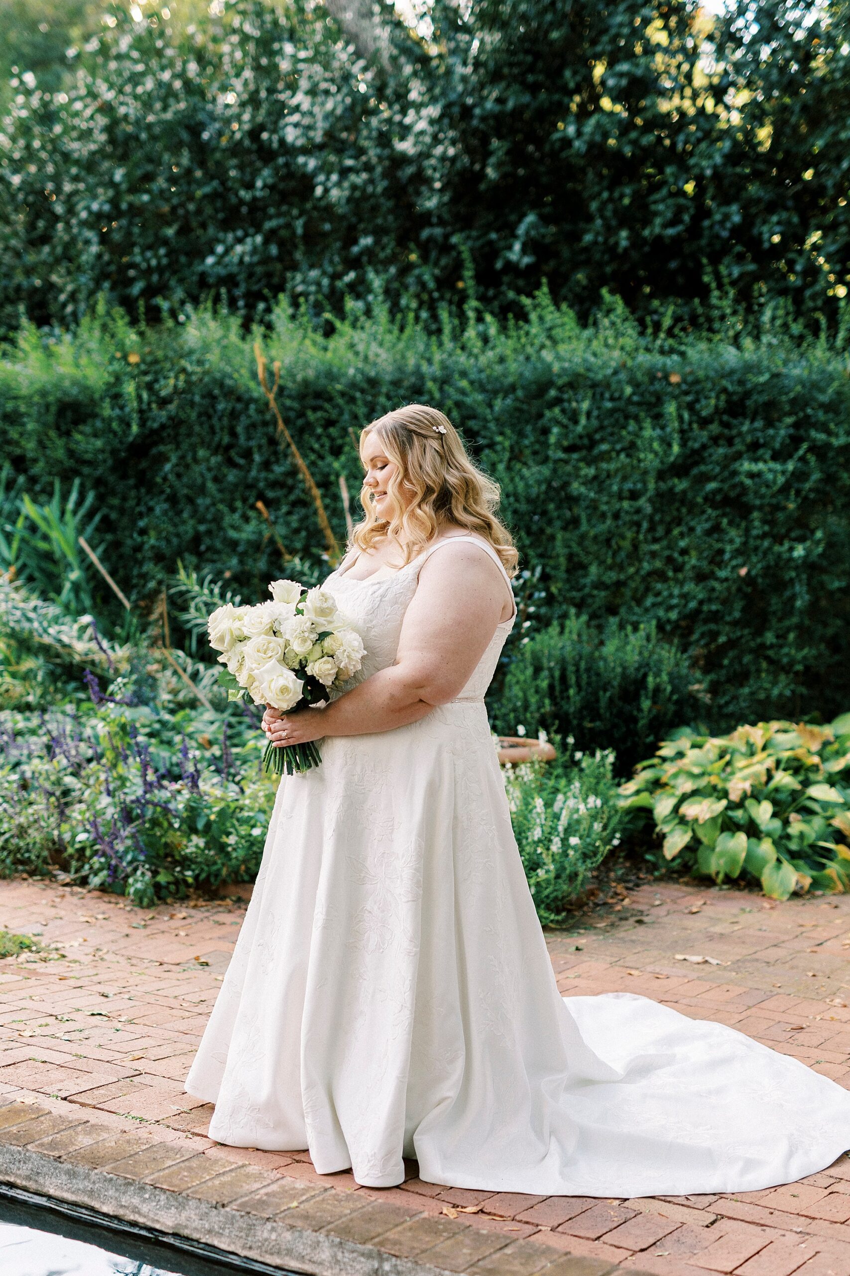 bride smiles down at ivory roses inside Wing Haven Gardens