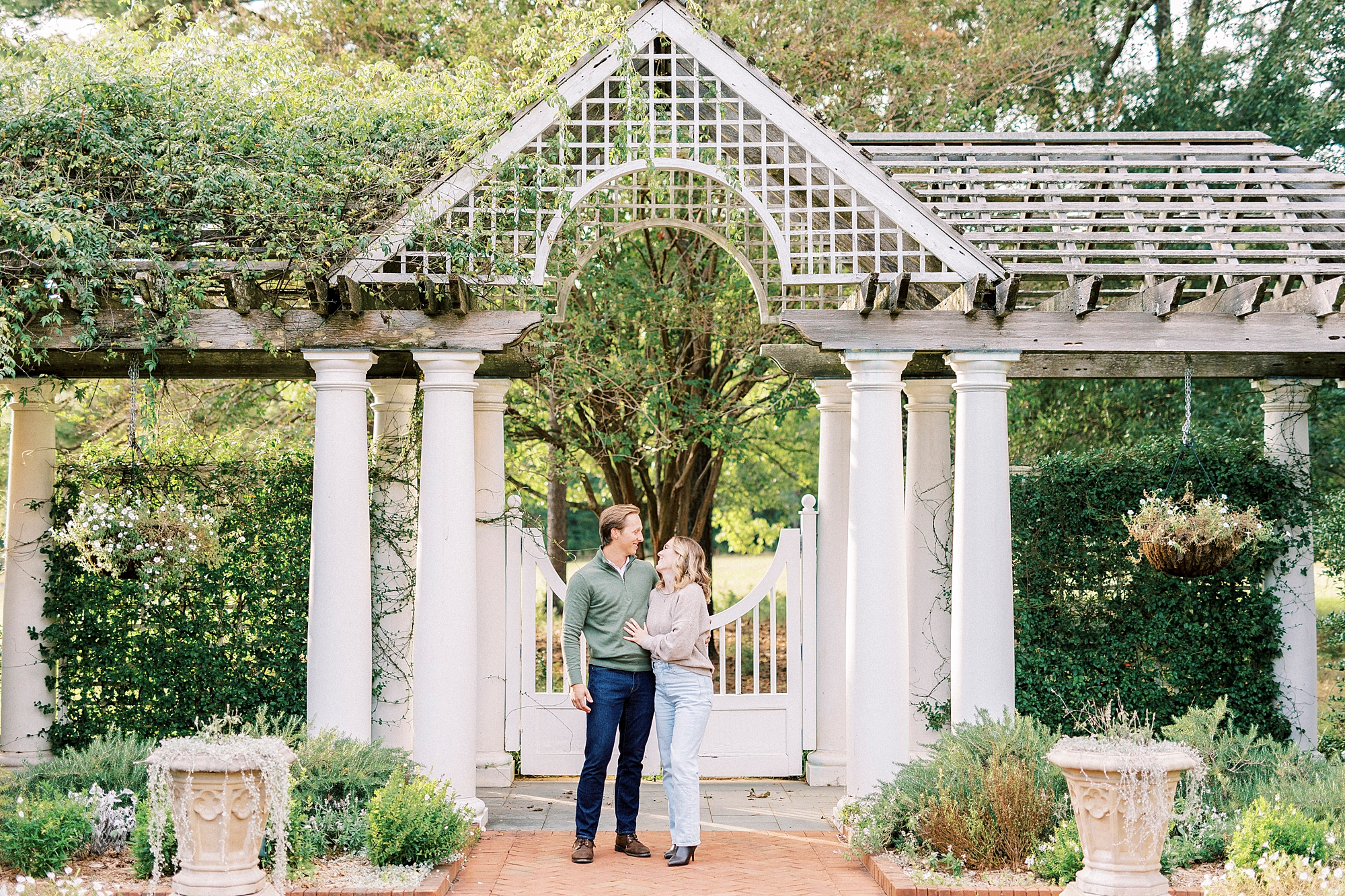 man and woman stand smiling at each other under arbor at Daniel Stowe Botanical Garden