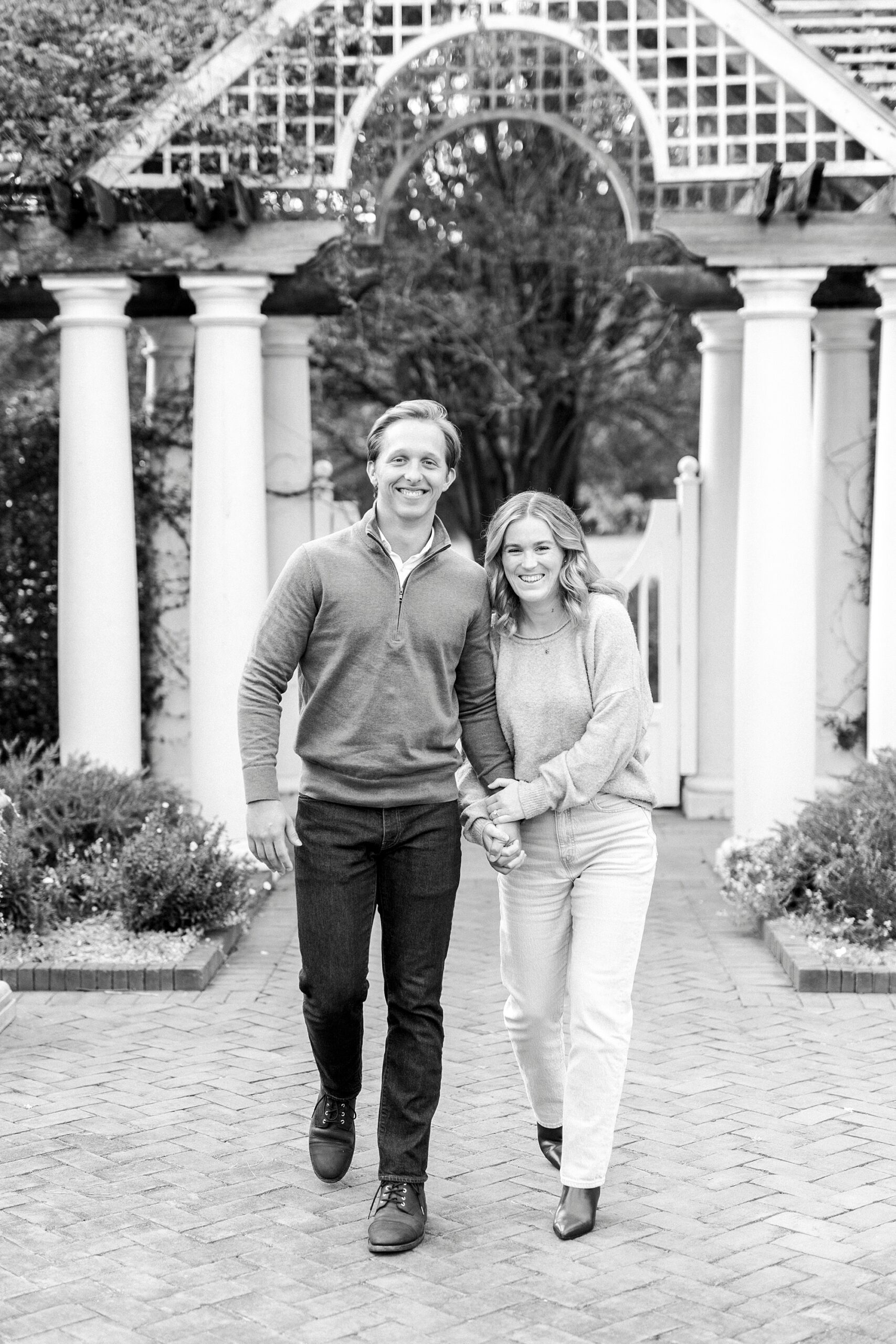 engaged couple holds hands walking by entrance at Daniel Stowe Botanical Garden