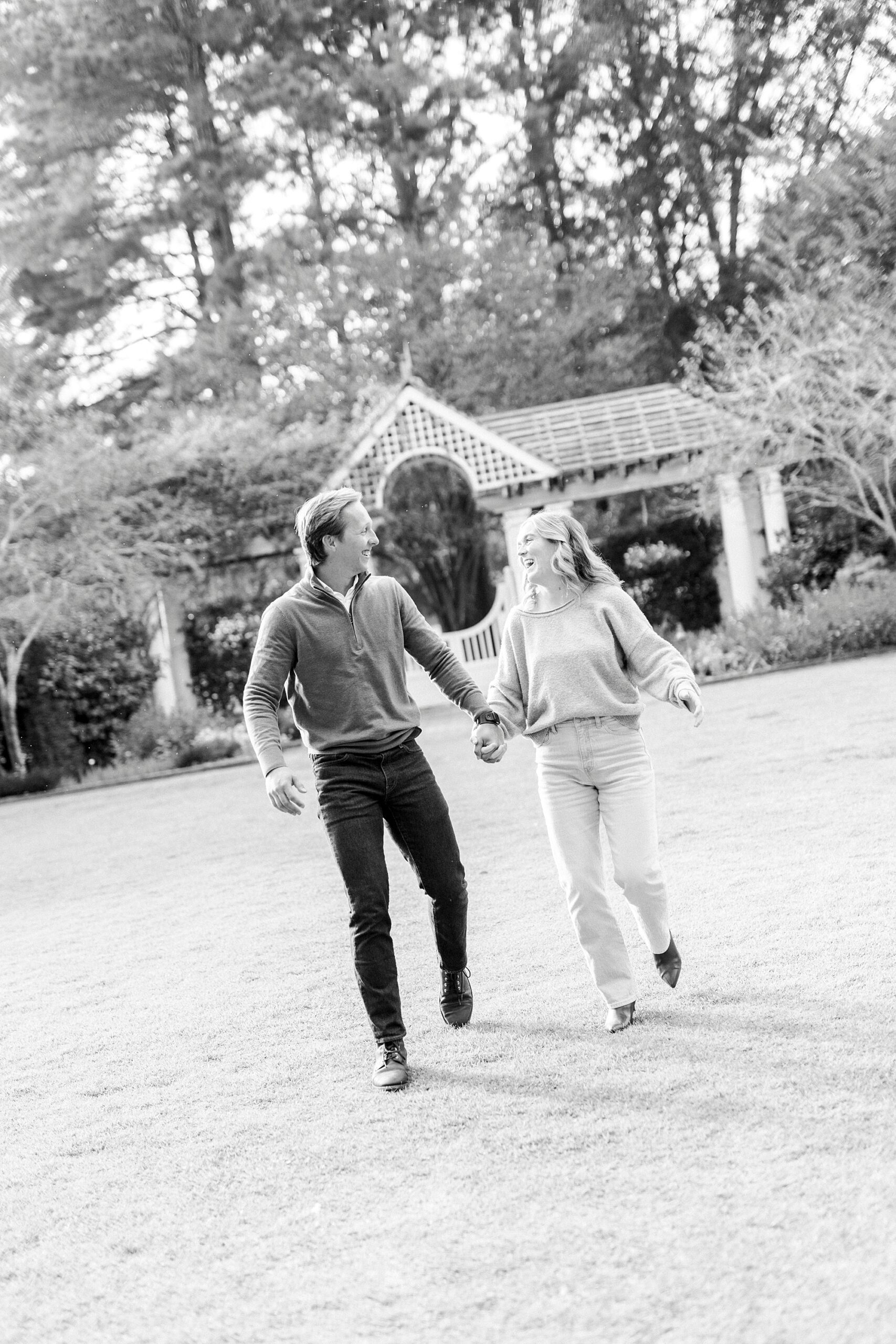 man and woman hold hands walking across brick patio in gardens