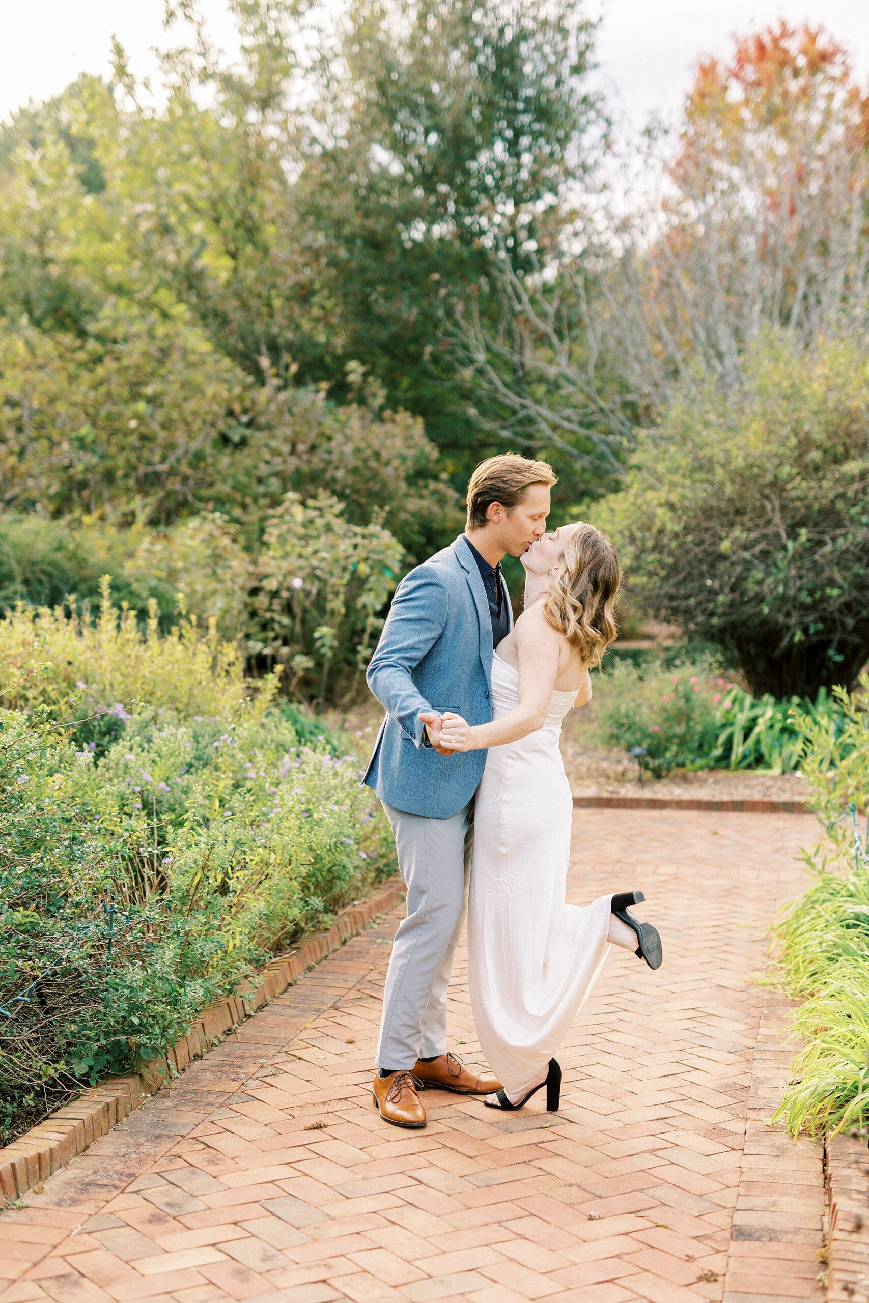 man and woman kiss on brick pathway inside Daniel Stowe Botanical Garden