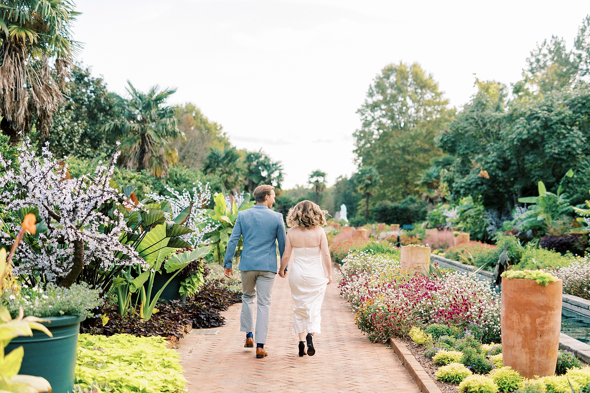 engaged couple holds hands walking through flowers at Daniel Stowe Botanical Garden