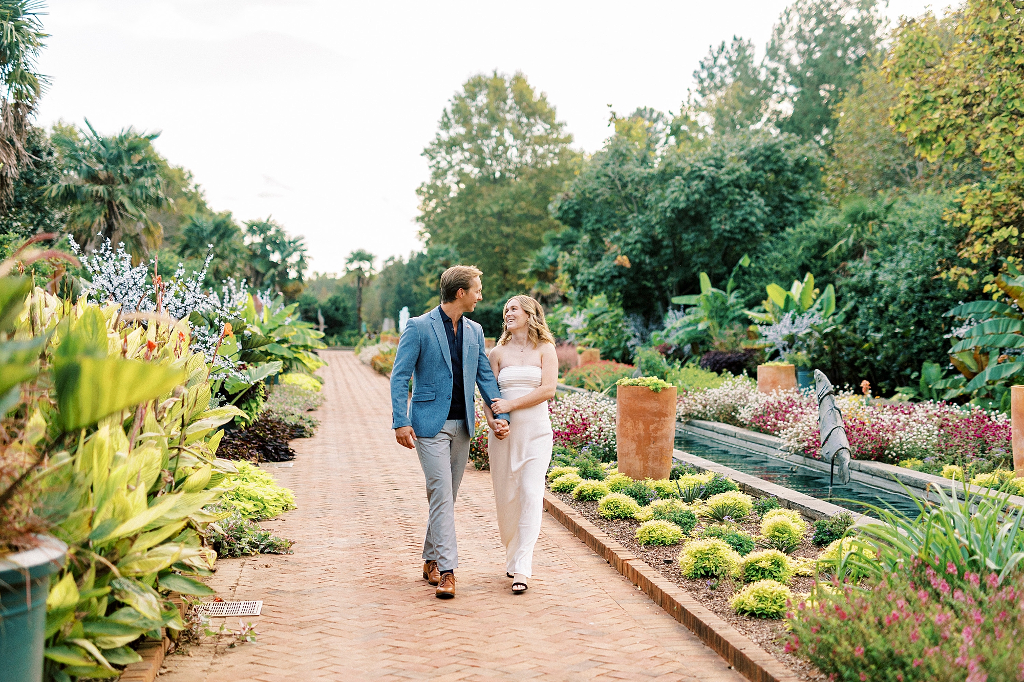 couple holds hands walking down row of flowers inside Daniel Stowe Botanical Garden