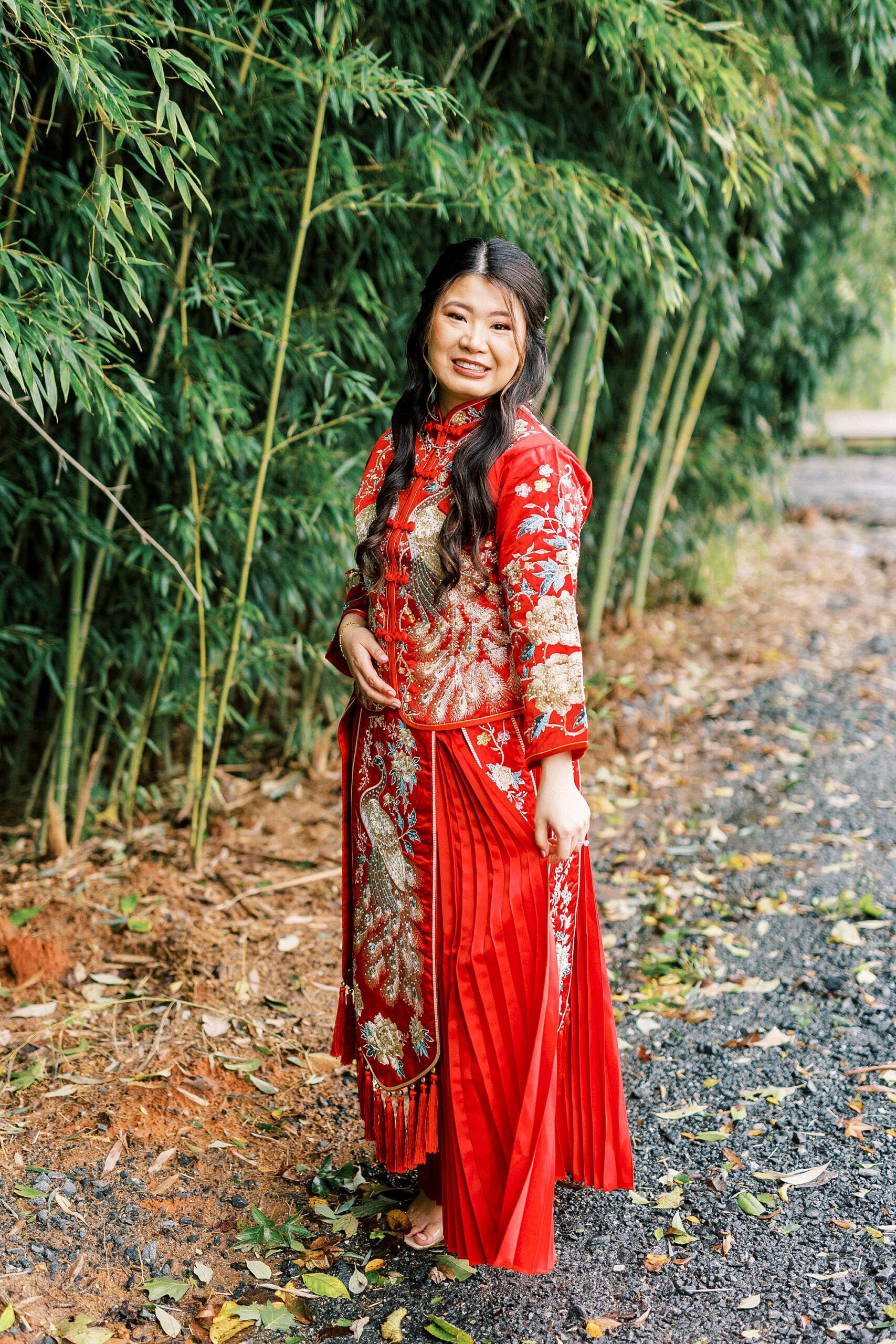 bride poses in red and gold Chinese attire inside bamboo forest at Camelot Meadows