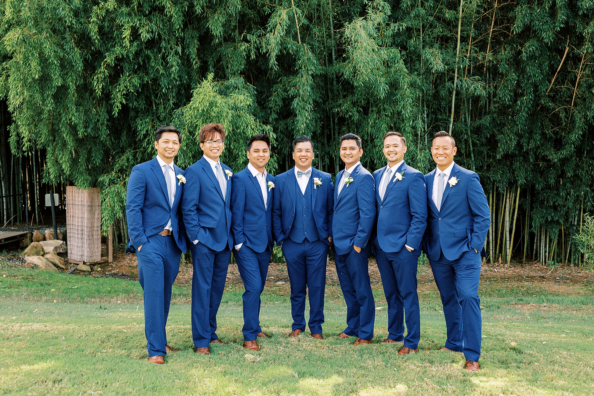 groom and groomsmen stand in blue suits on lawn at Camelot Meadows
