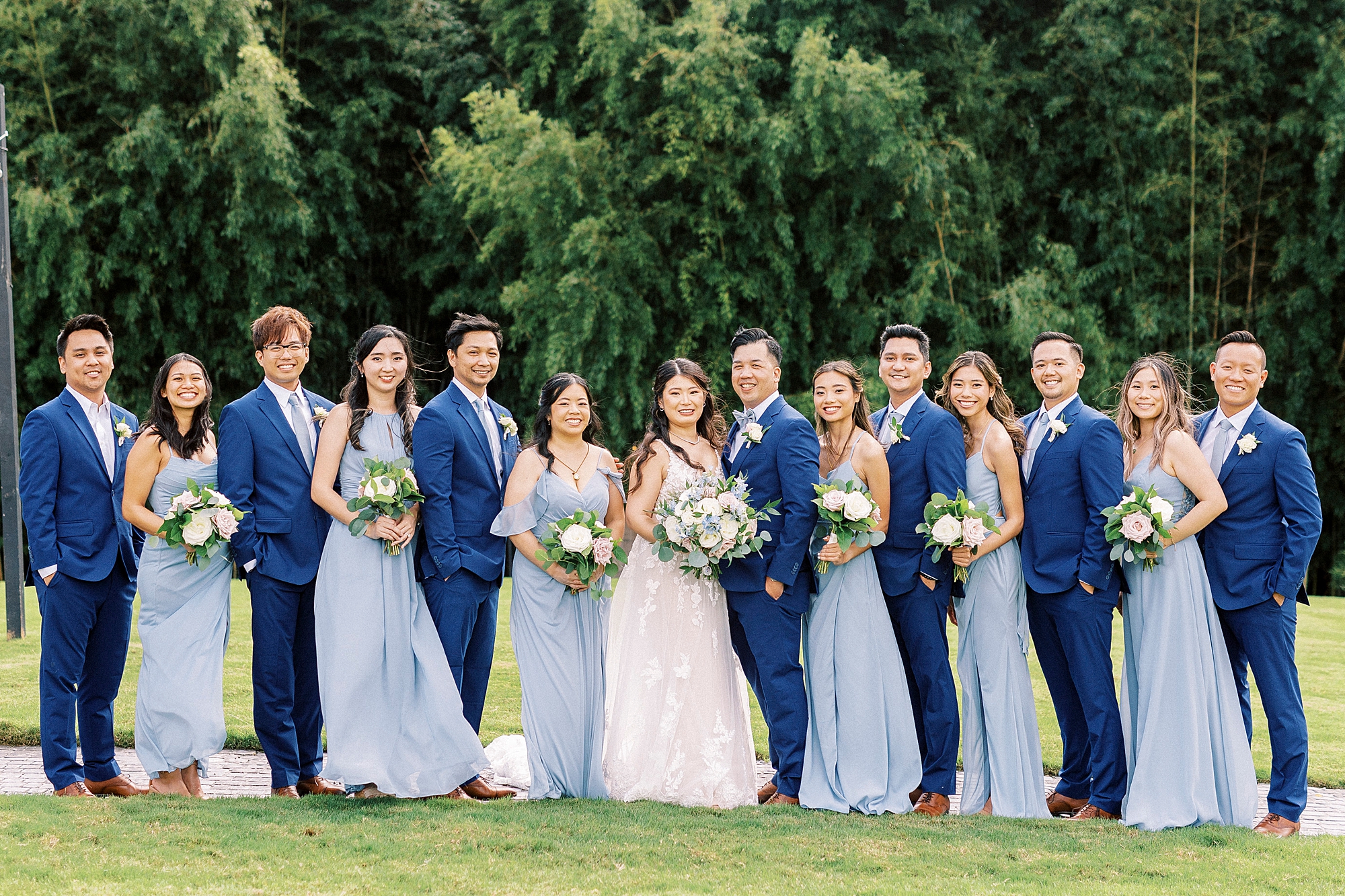 bride and groom stand with wedding party in light blue dresses sand blue suits 