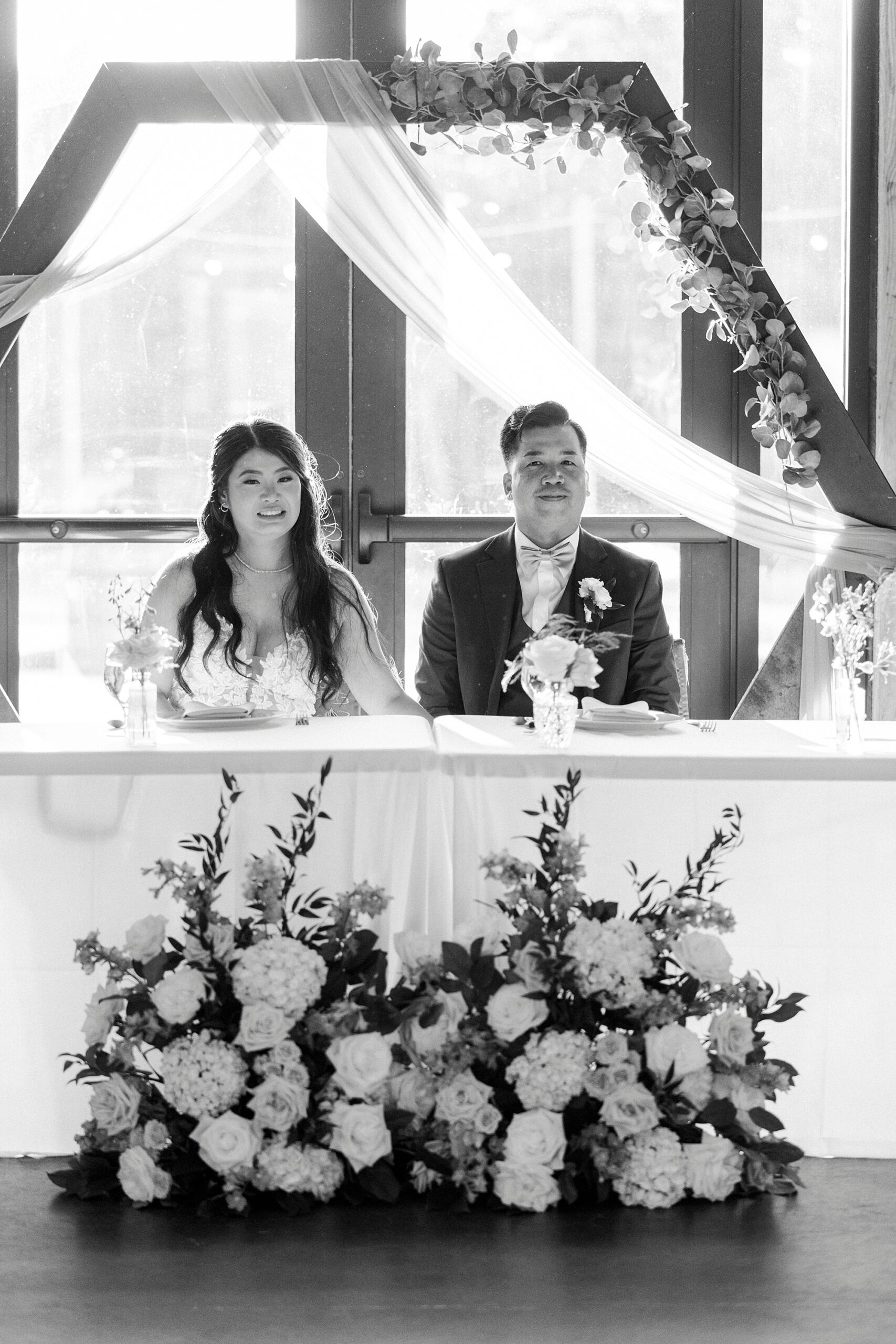 bride and groom sit at sweetheart table with florals in front of them at Camelot Meadows