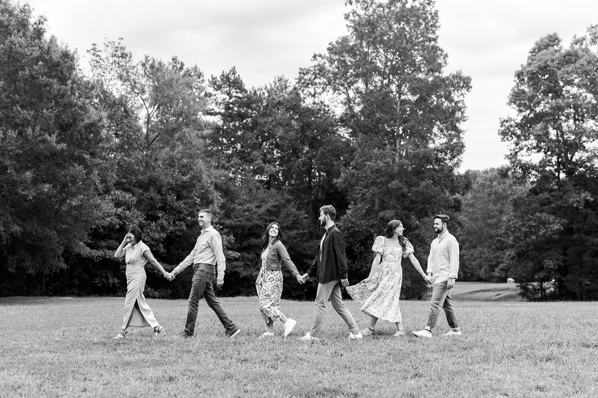 couples hold hands walking in front of trees at Rob Wallace Park