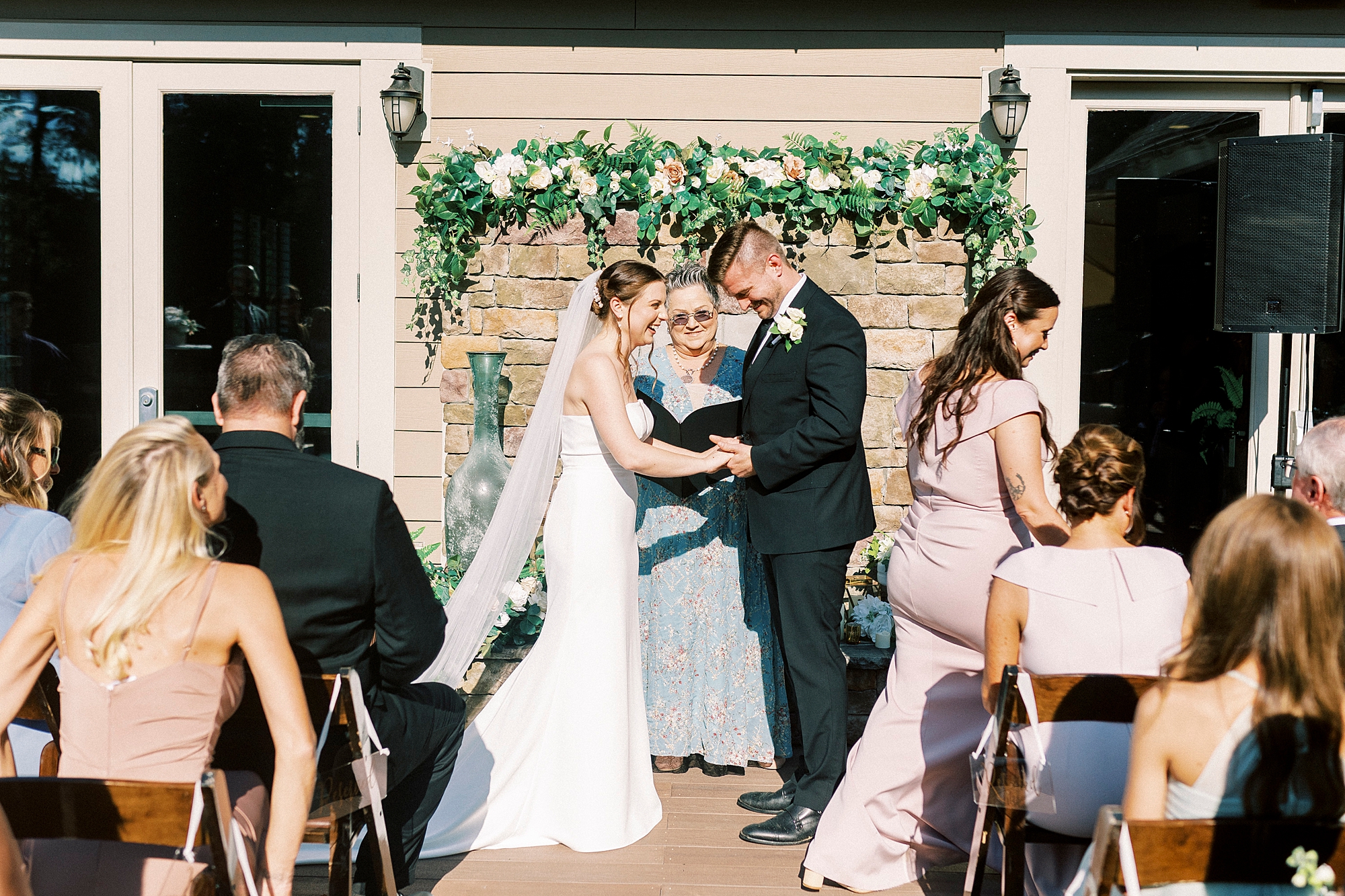 bride and groom laugh during wedding ceremony in front of brick fireplace at Palisades Country Club