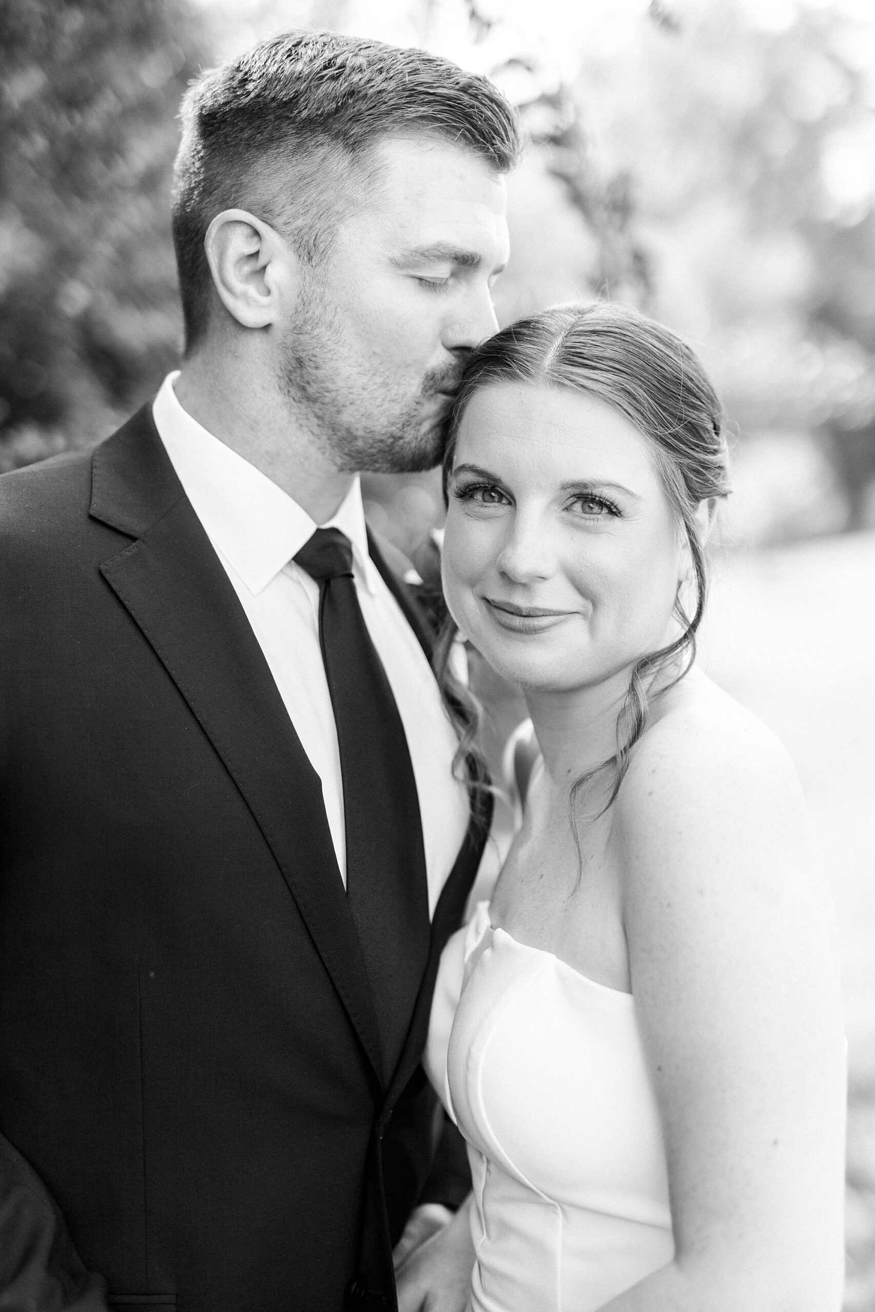 black and white photo of groom kissing bride's forehead 