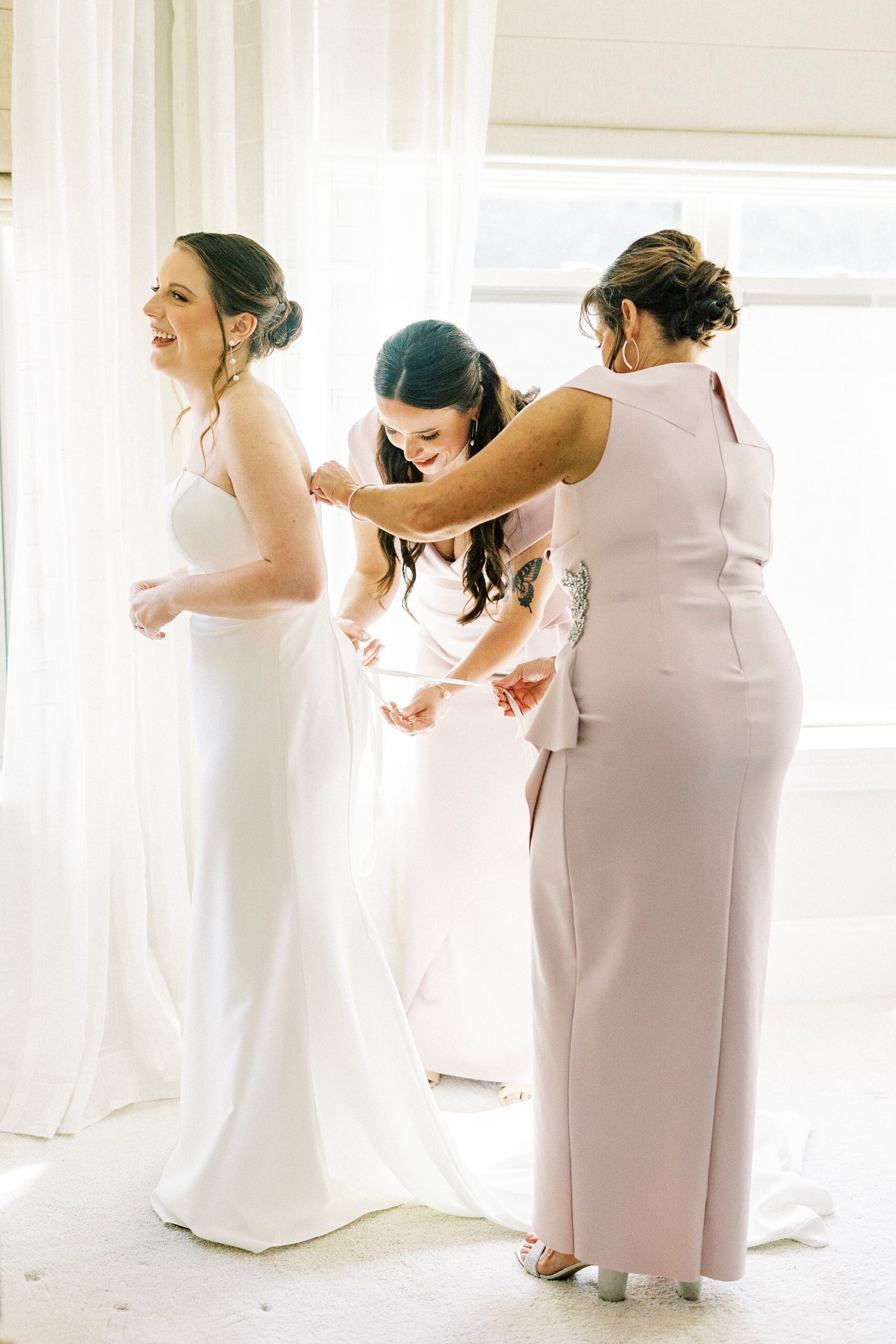 bridesmaid and mother help bride into wedding gown