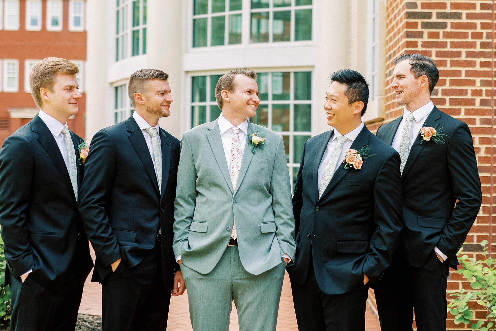groom stands with groomsmen outside the atrium at Belk Chapel at Queens University