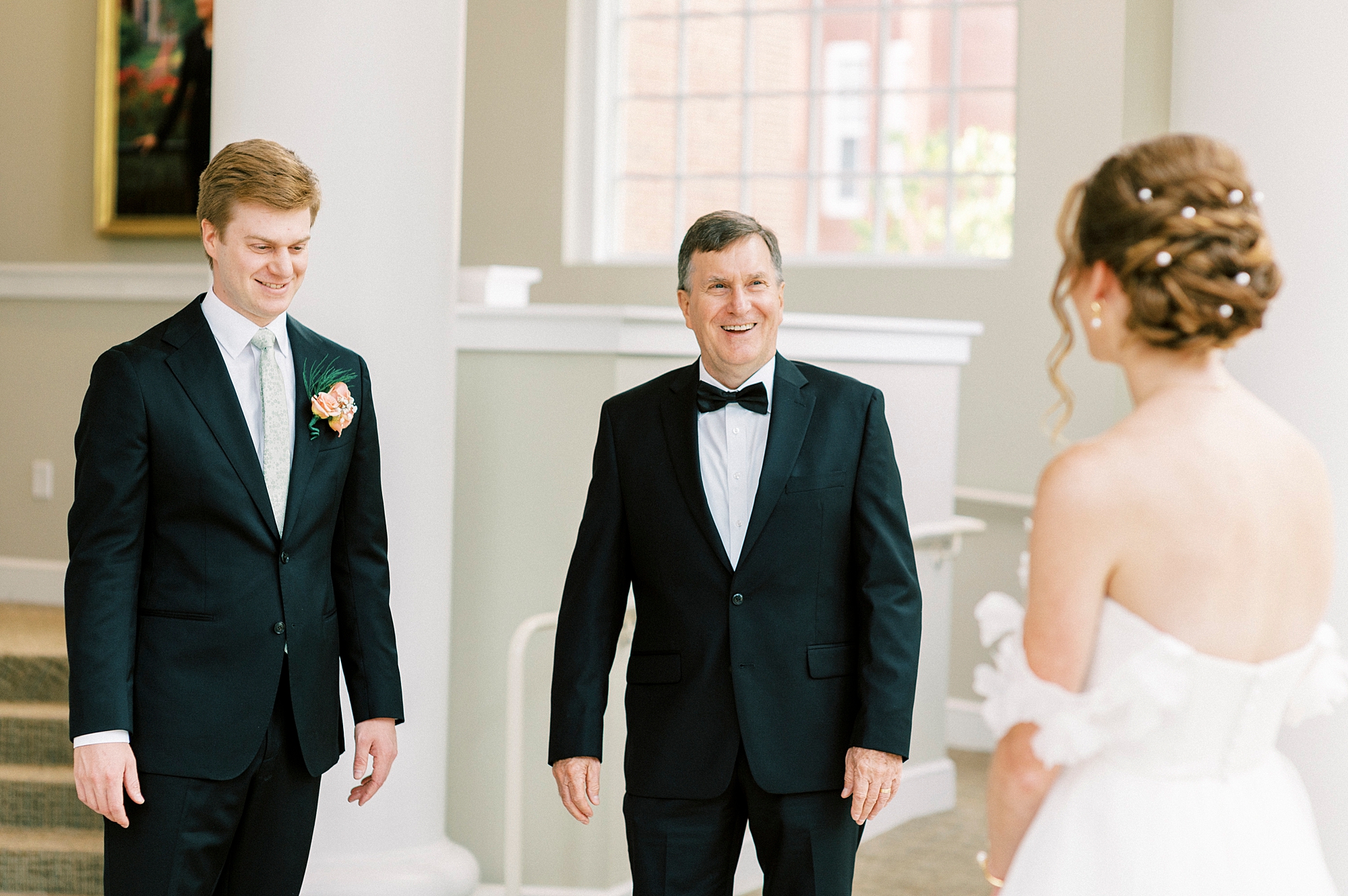 bride has first look with dad and brother inside atrium of the Belk Chapel