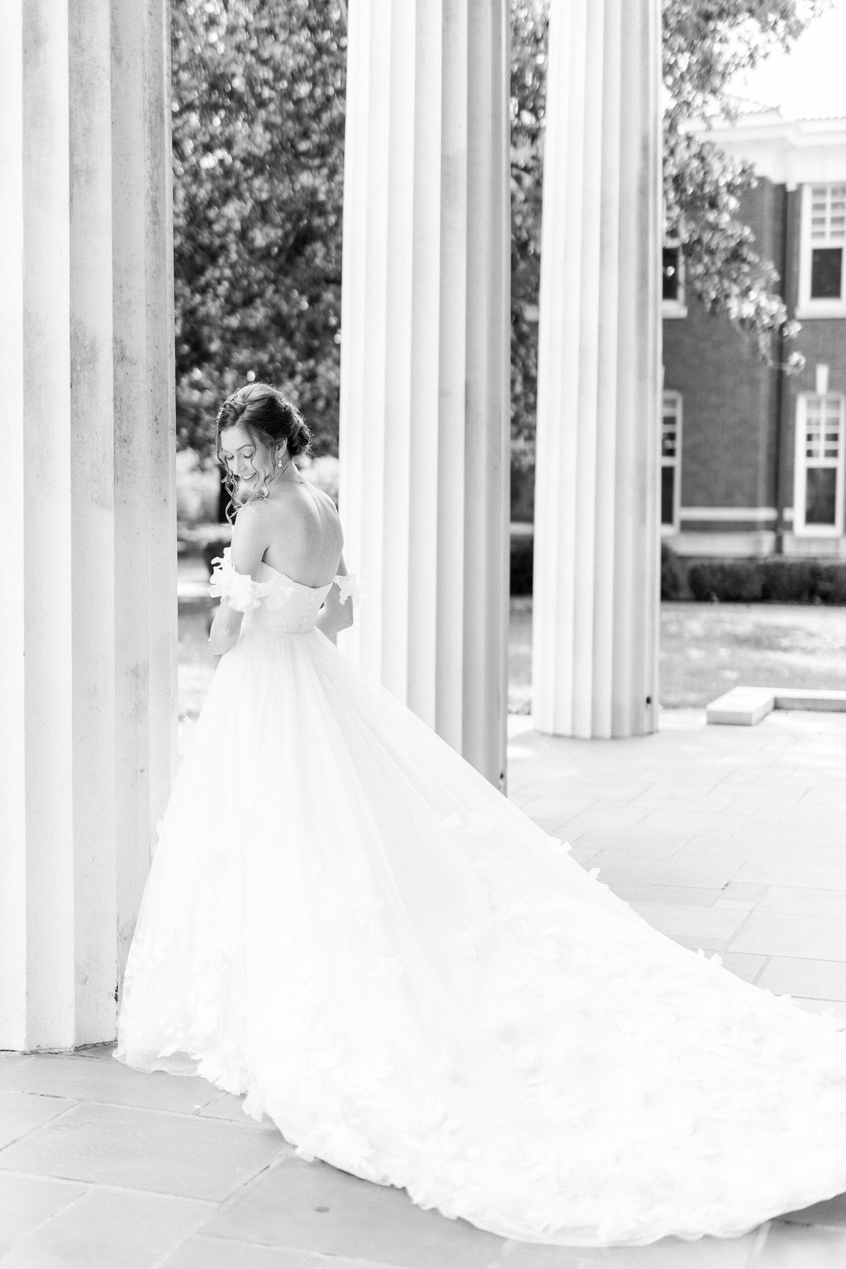 bride stands near pillar at Belk Chapel with dress pulled out behind her