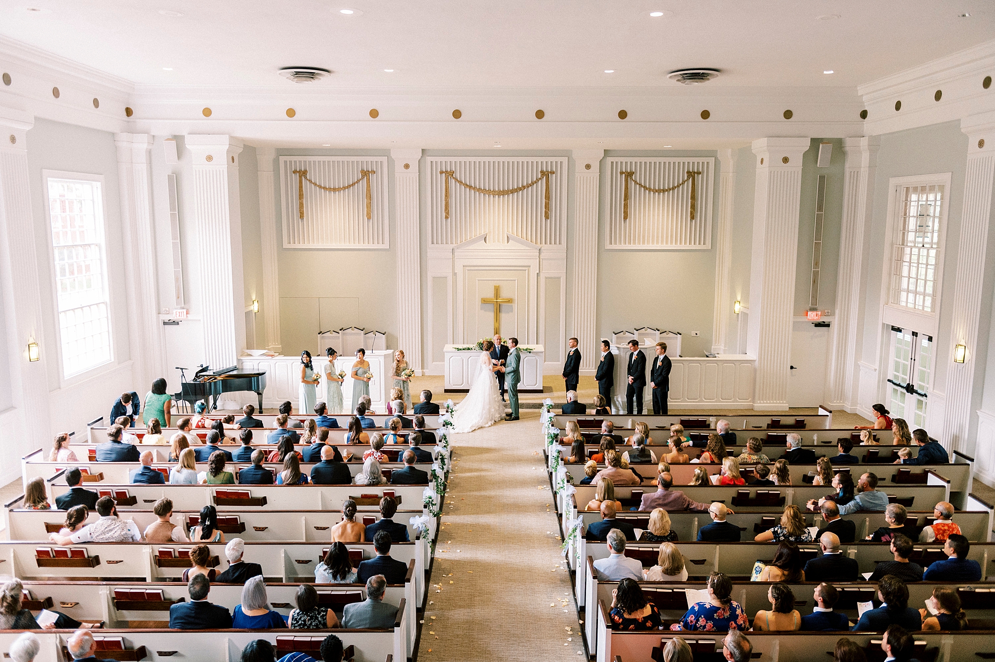 wide photo of bride and groom with guests inside Belk Chapel