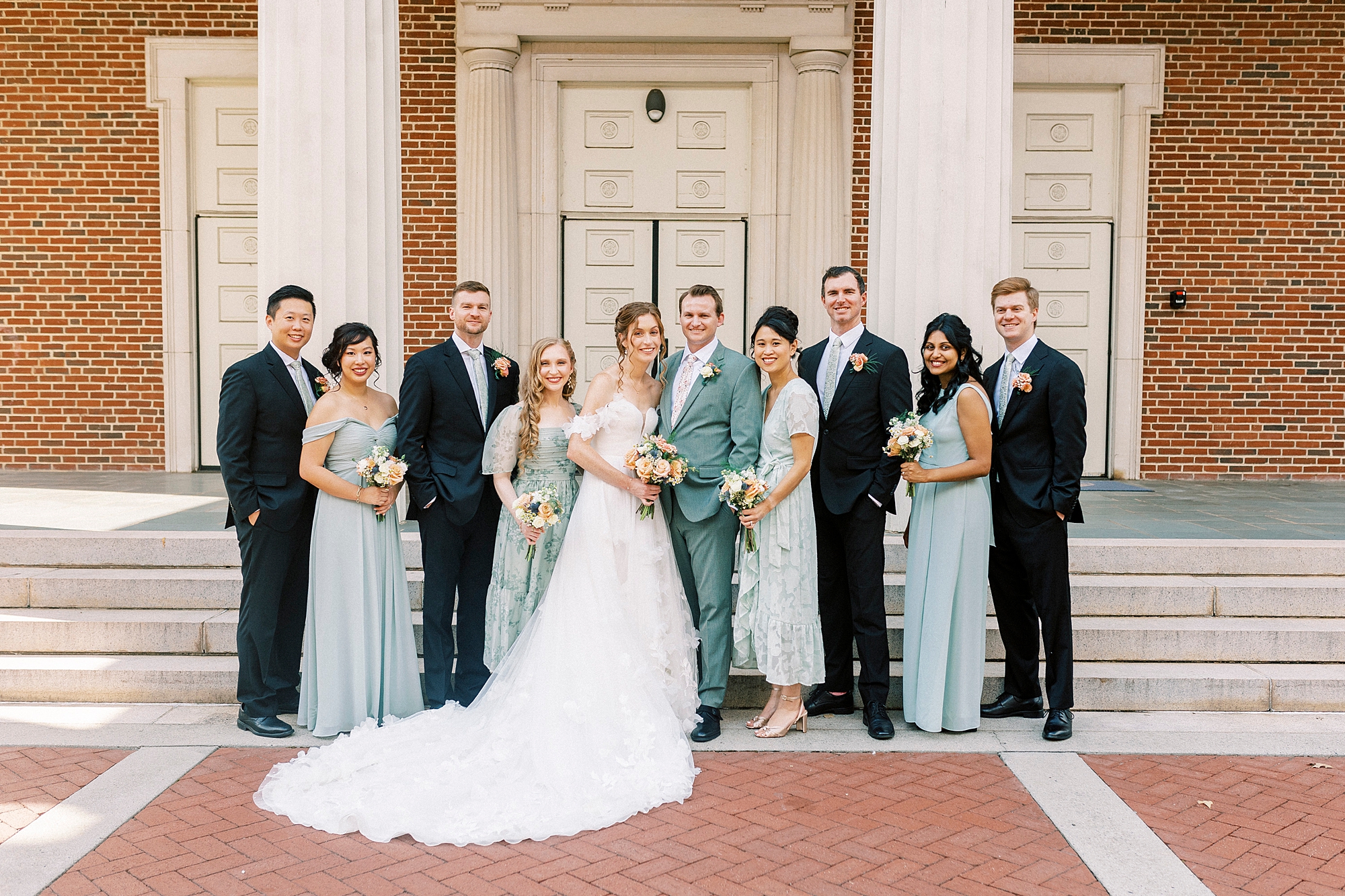 bride and groom stand with wedding party in blue and black attire outside Belk Chapel