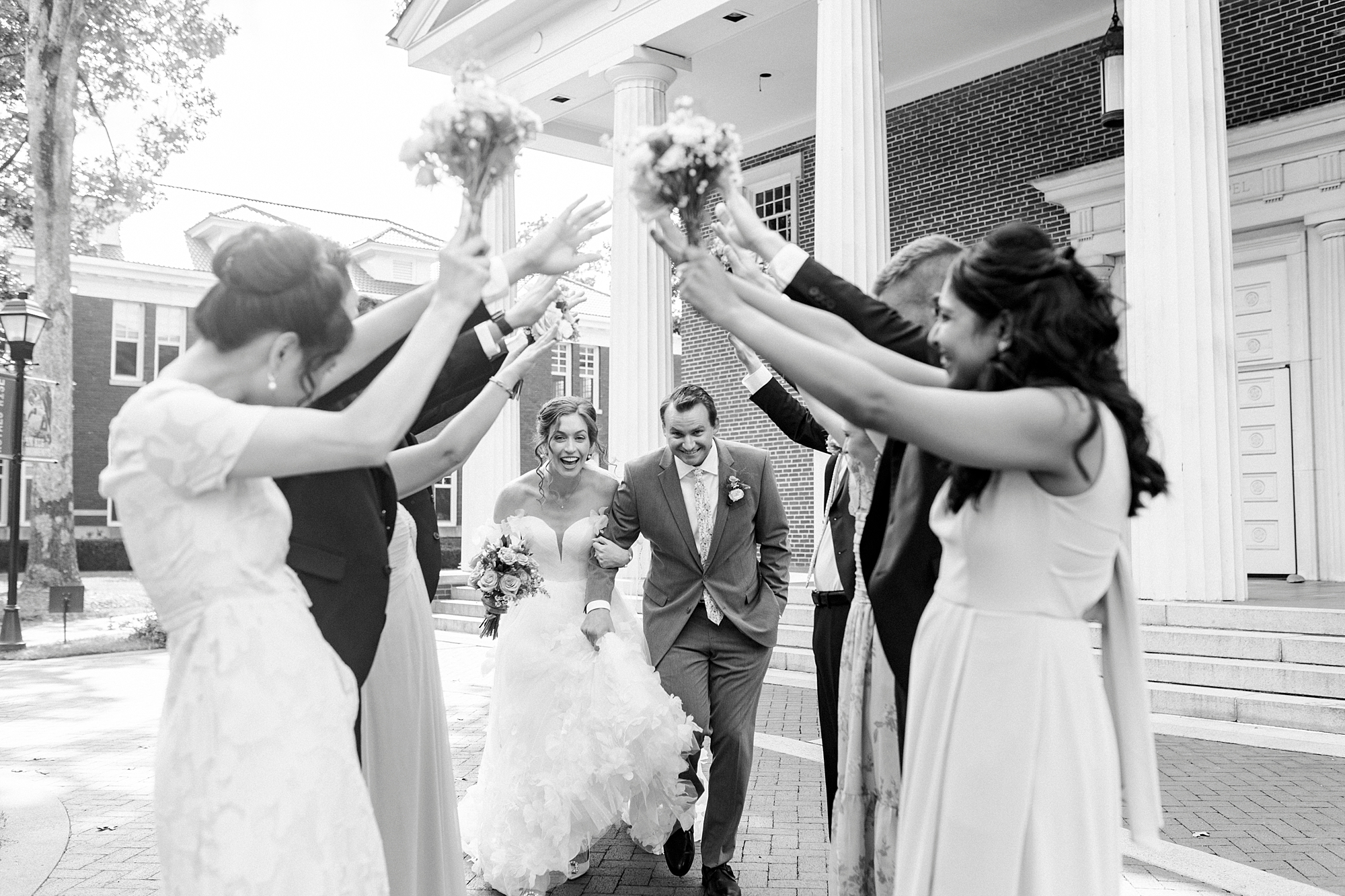 newlyweds walk through tunnel made from bridal party outside Belk Chapel