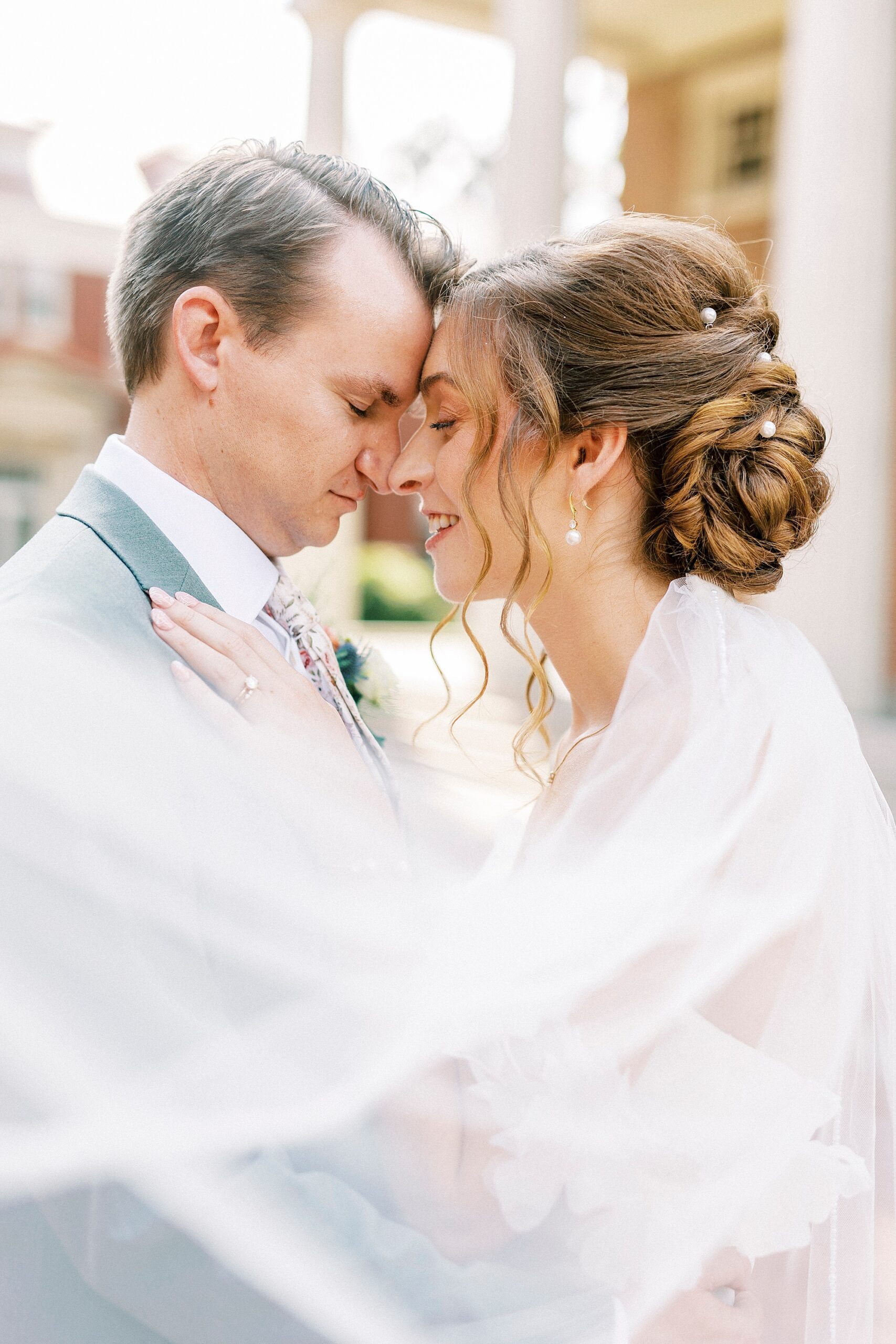 bride and groom lean heads together with veil around them outside Belk Chapel in Charlotte NC