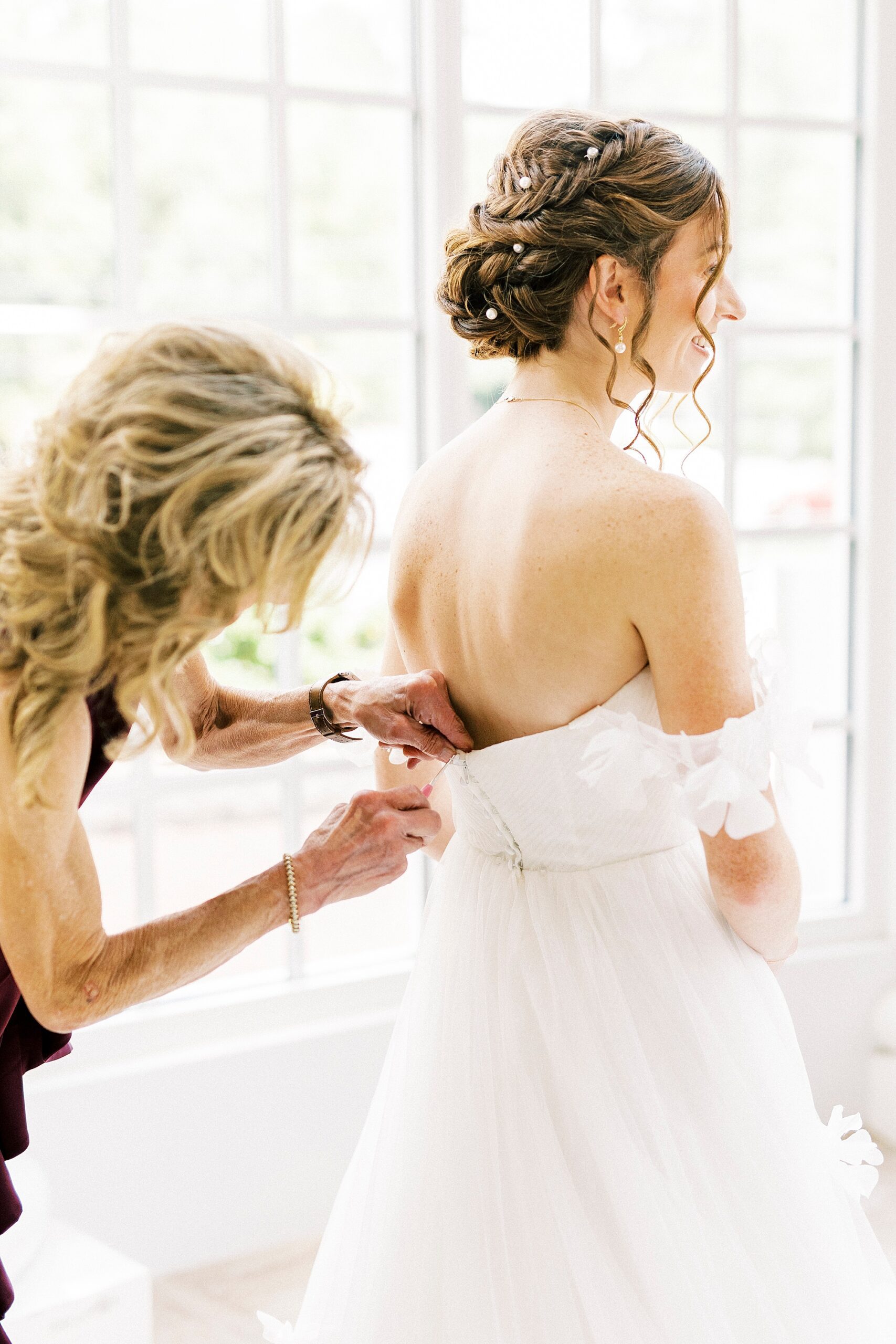 mother helps bride into wedding dress inside the atrium at Belk Chapel