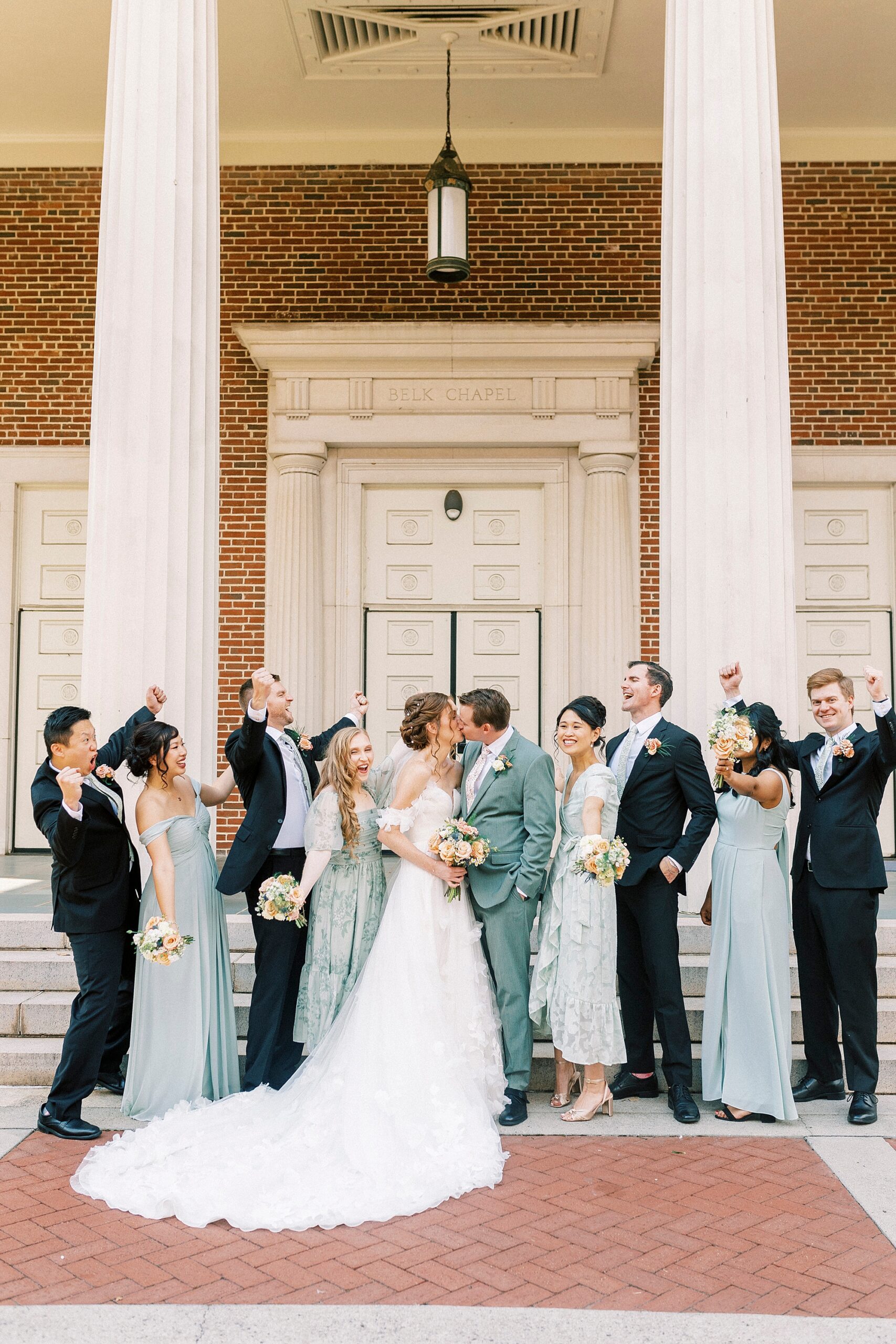 newlyweds kiss outside Belk Chapel with wedding party around them
