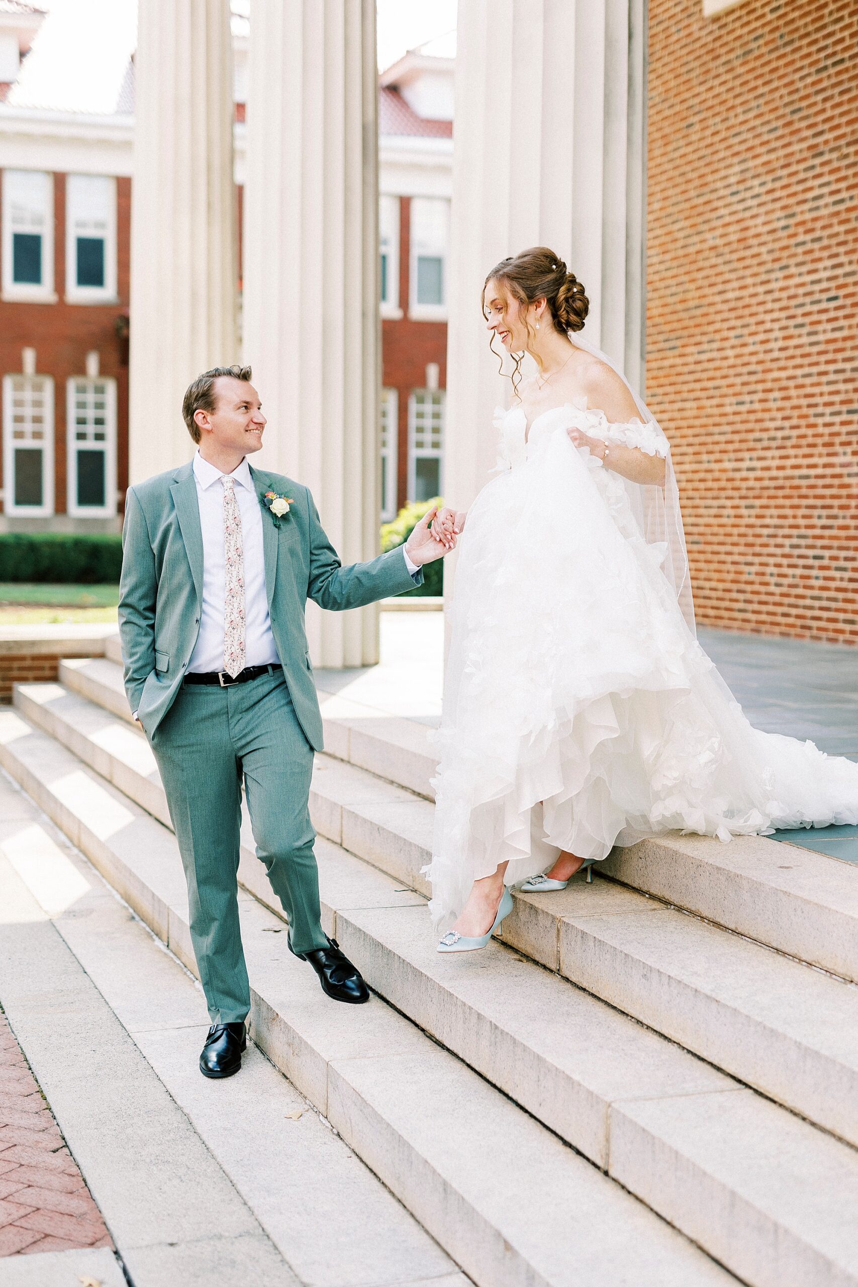 groom leads bride down steps outside Belk Chapel at Queens University