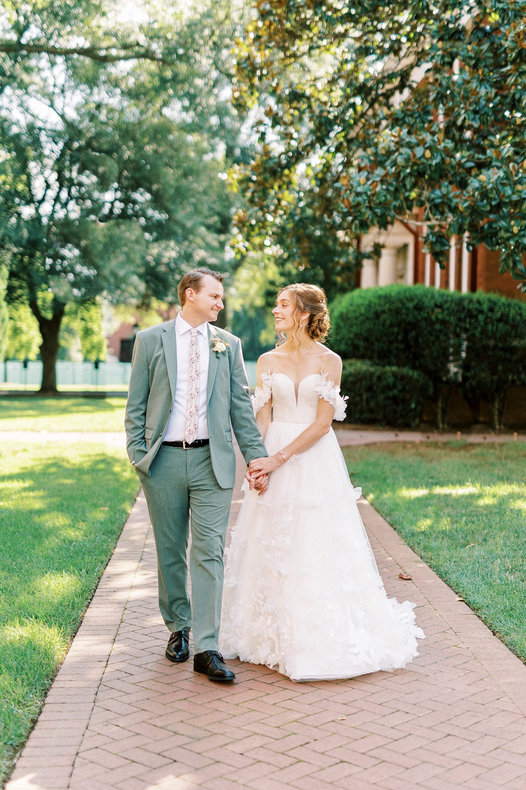 newlyweds hold hands walking across lawn at Belk Chapel at Queens University