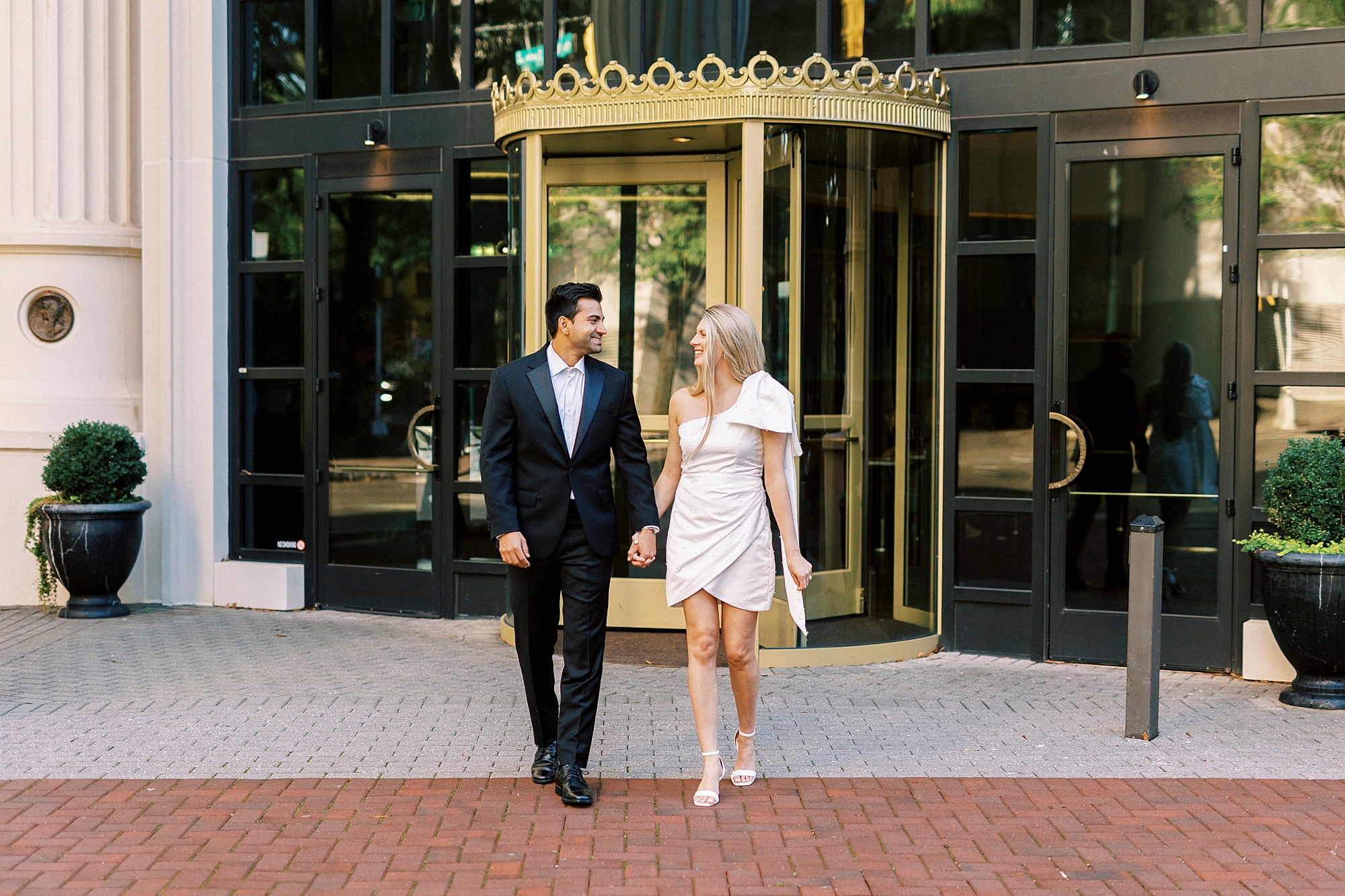 man and woman hold hands walking in front of gold doors at the Grand Bohemian Hotel in Charlotte NC